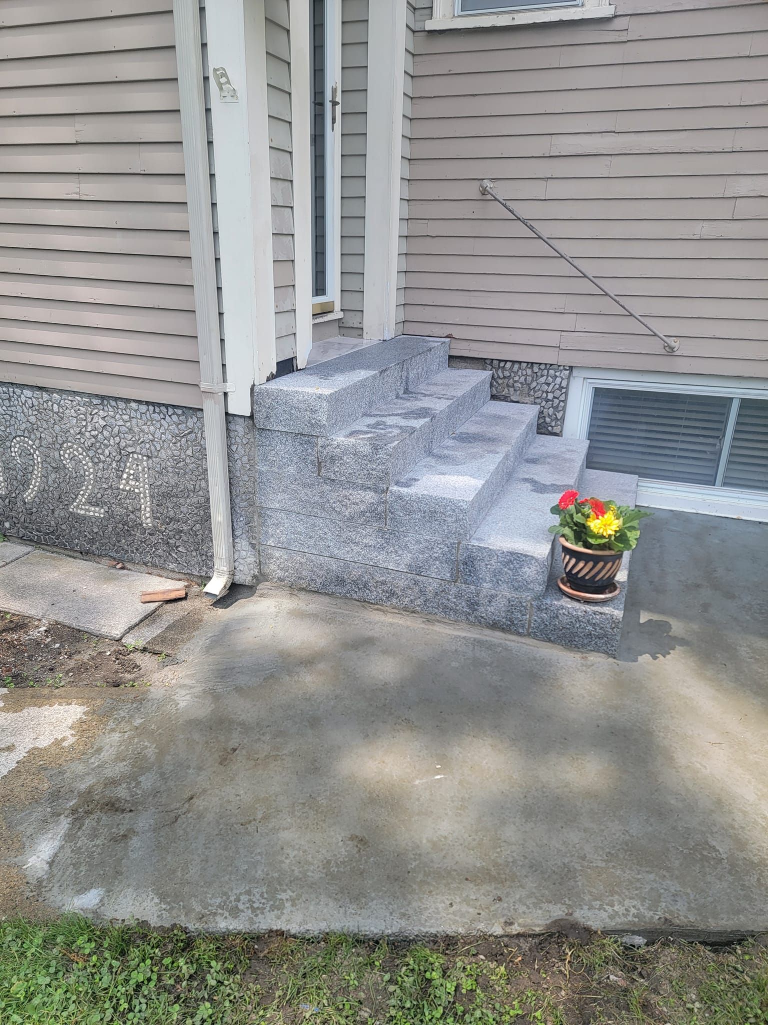 Exterior view of a house with concrete steps leading to the front door, a potted plant, and a gray siding.