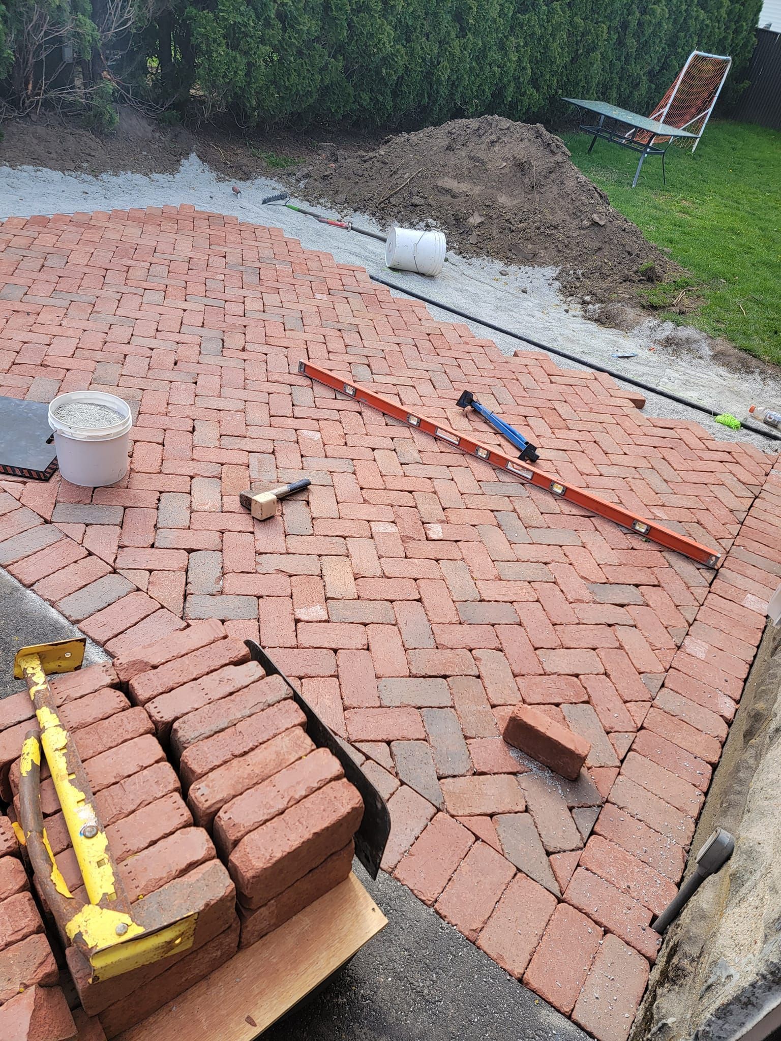 Brick patio under construction, reddish-brown bricks in herringbone pattern