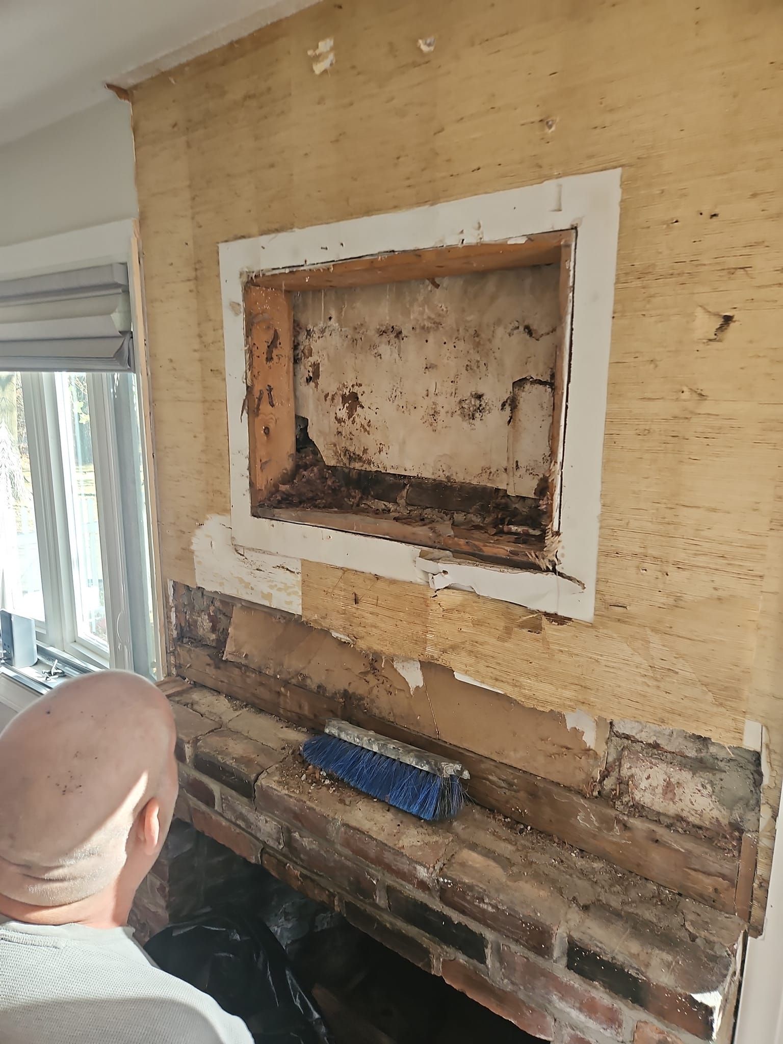 Man cleaning a brick fireplace. Recessed wooden alcove above the brick. Wall has exposed wood.