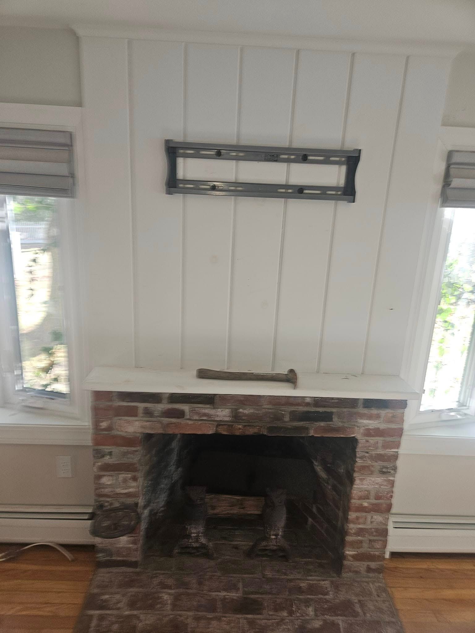 Fireplace with brick surround, white paneling above, and TV mount. Windows on either side.