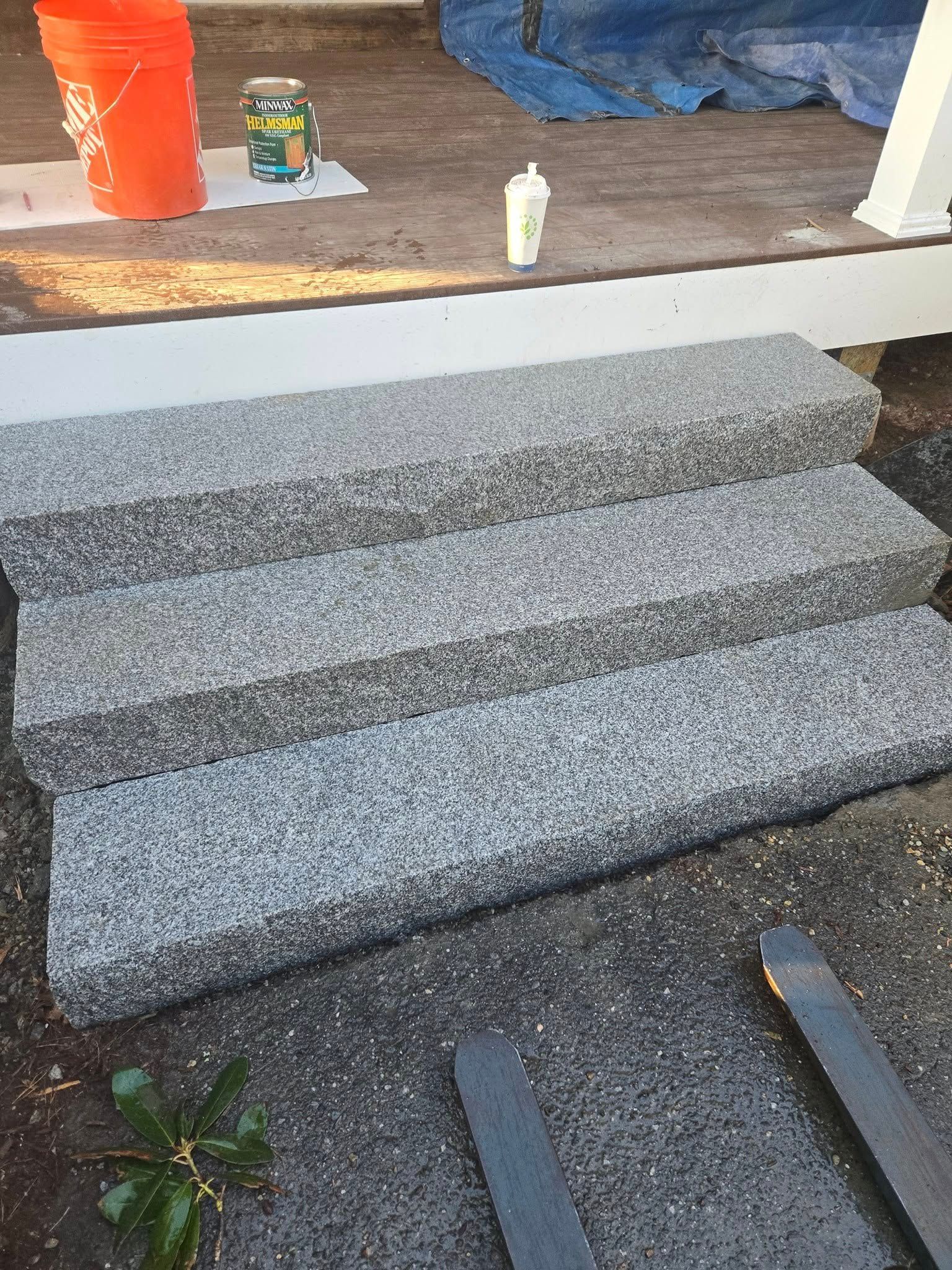 Three gray granite steps leading up to a porch, with a bucket and supplies in the background.
