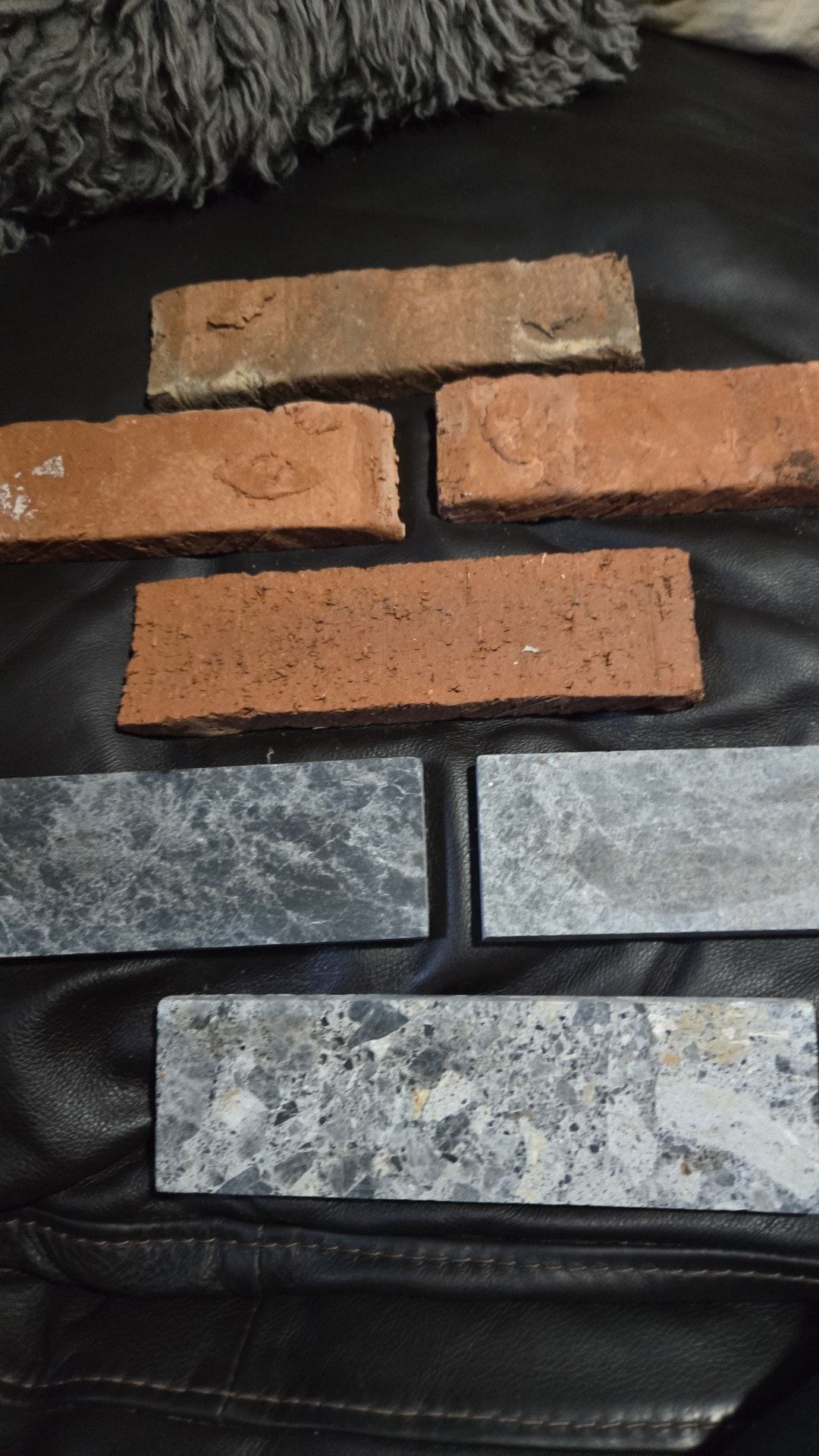 Six rectangular bricks, three red-brown and three gray-blue with speckled patterns, arranged on black surface.