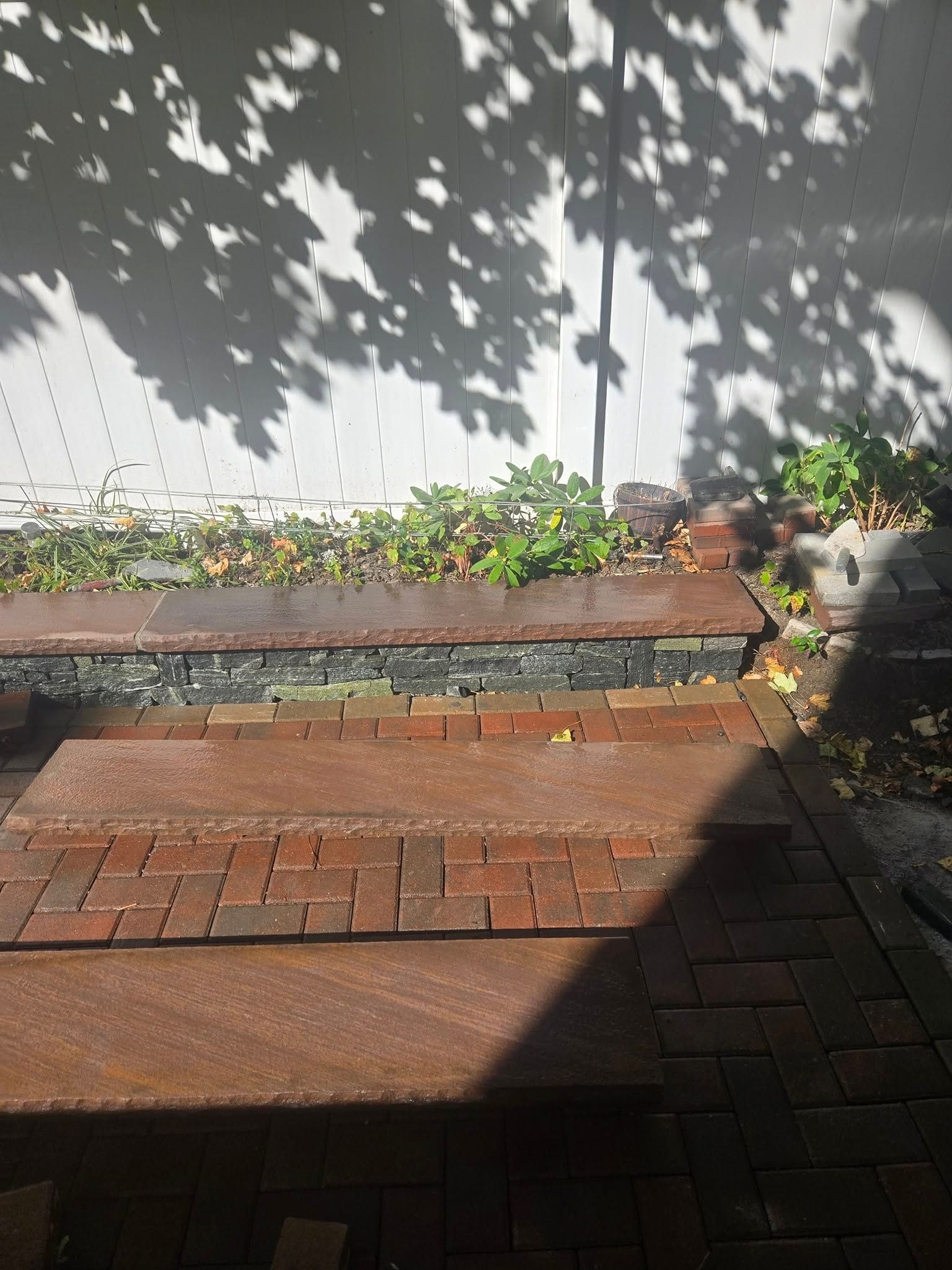 Brick patio with planter box against a white wall; shadows from foliage.