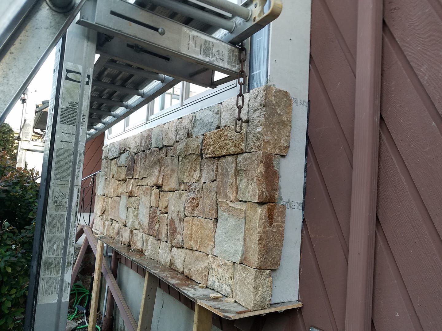 Stone wall being constructed on the side of a brown building, scaffolding present.