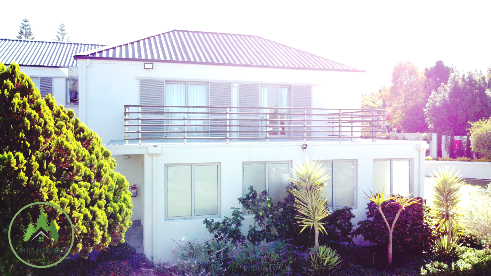 Een wit huis met een zwart dak is omgeven door bomen en struiken