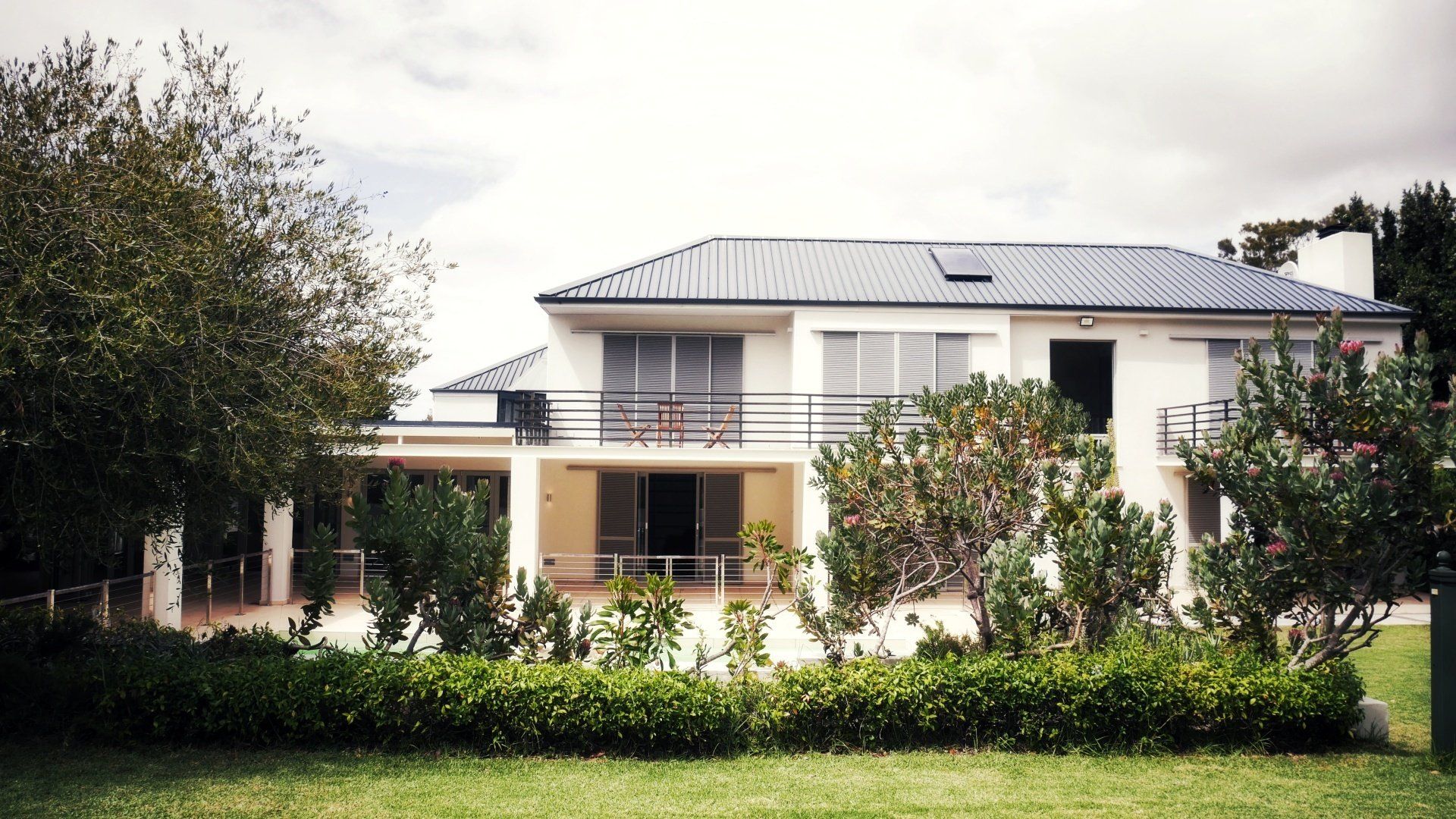 Een groot wit huis met een blauw dak is omgeven door bomen en struiken