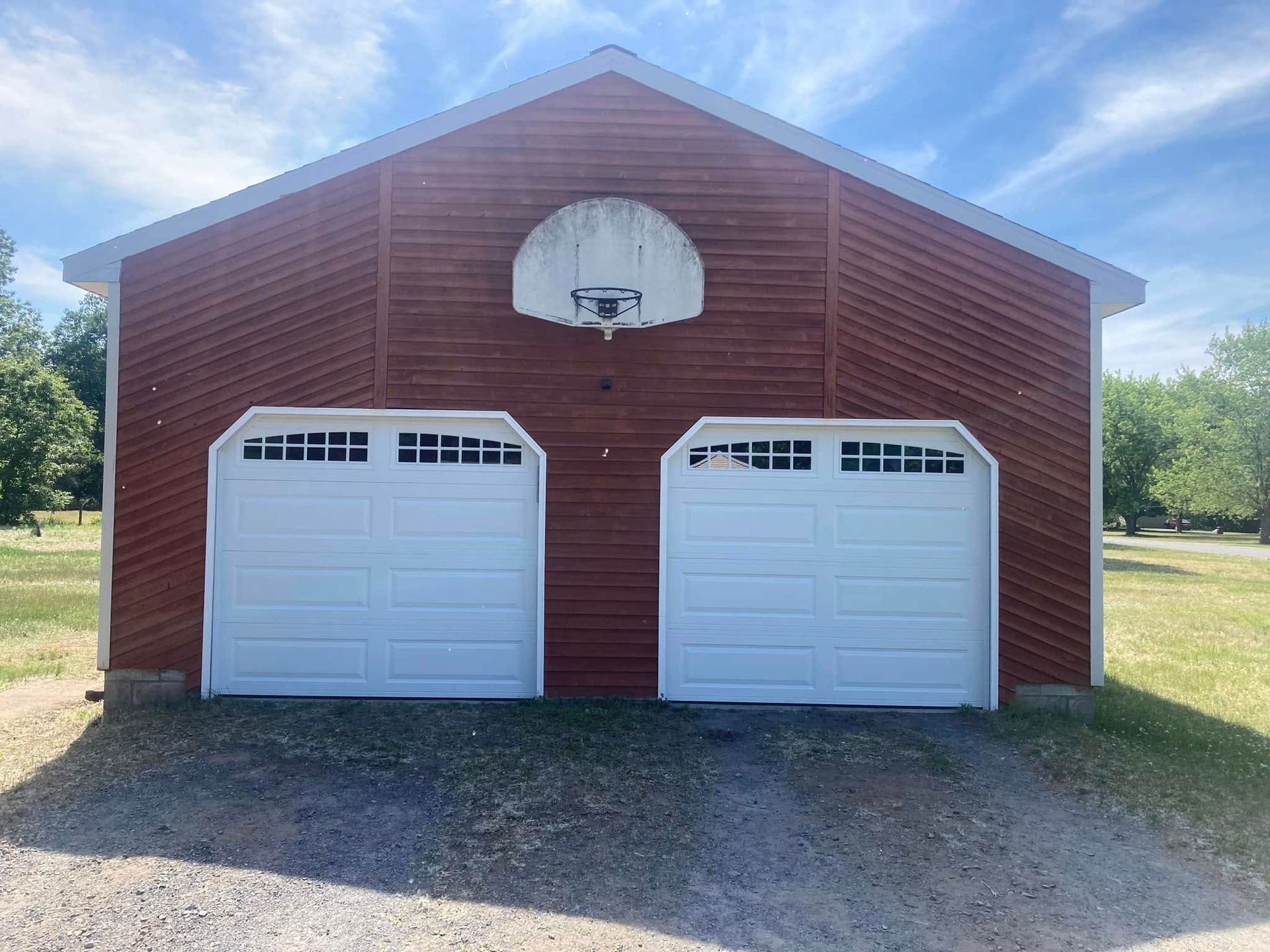 Red garage with two white garage doors and a basketball hoop.