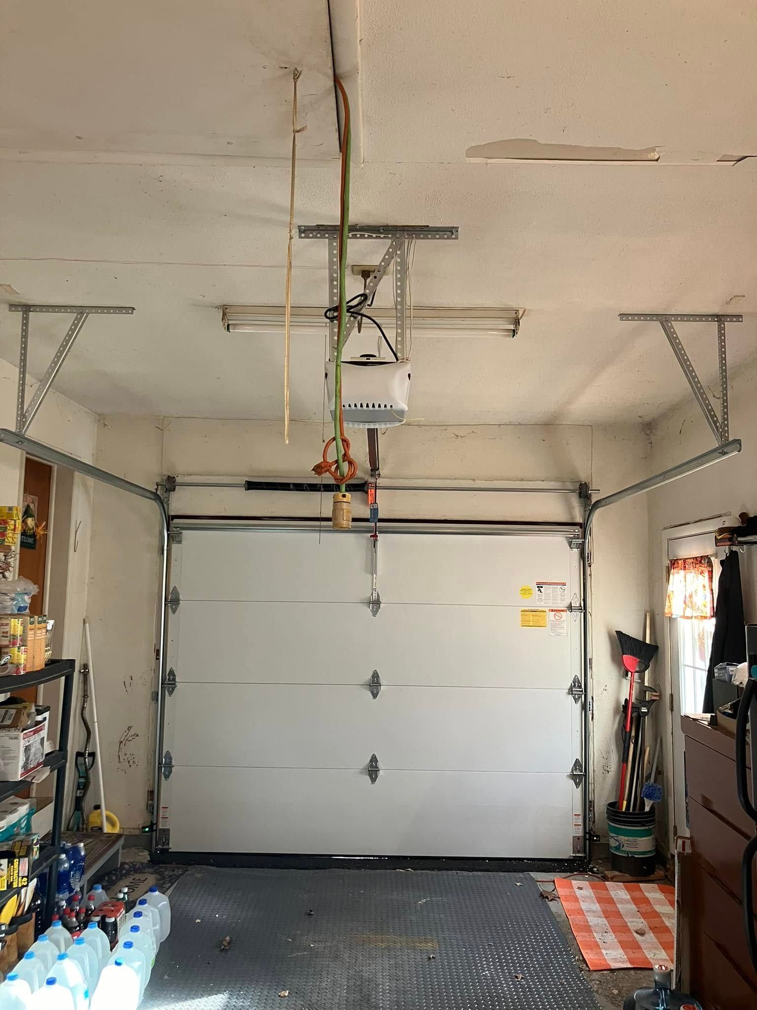 Garage door, white, closed, with opener on ceiling, items stored along walls.