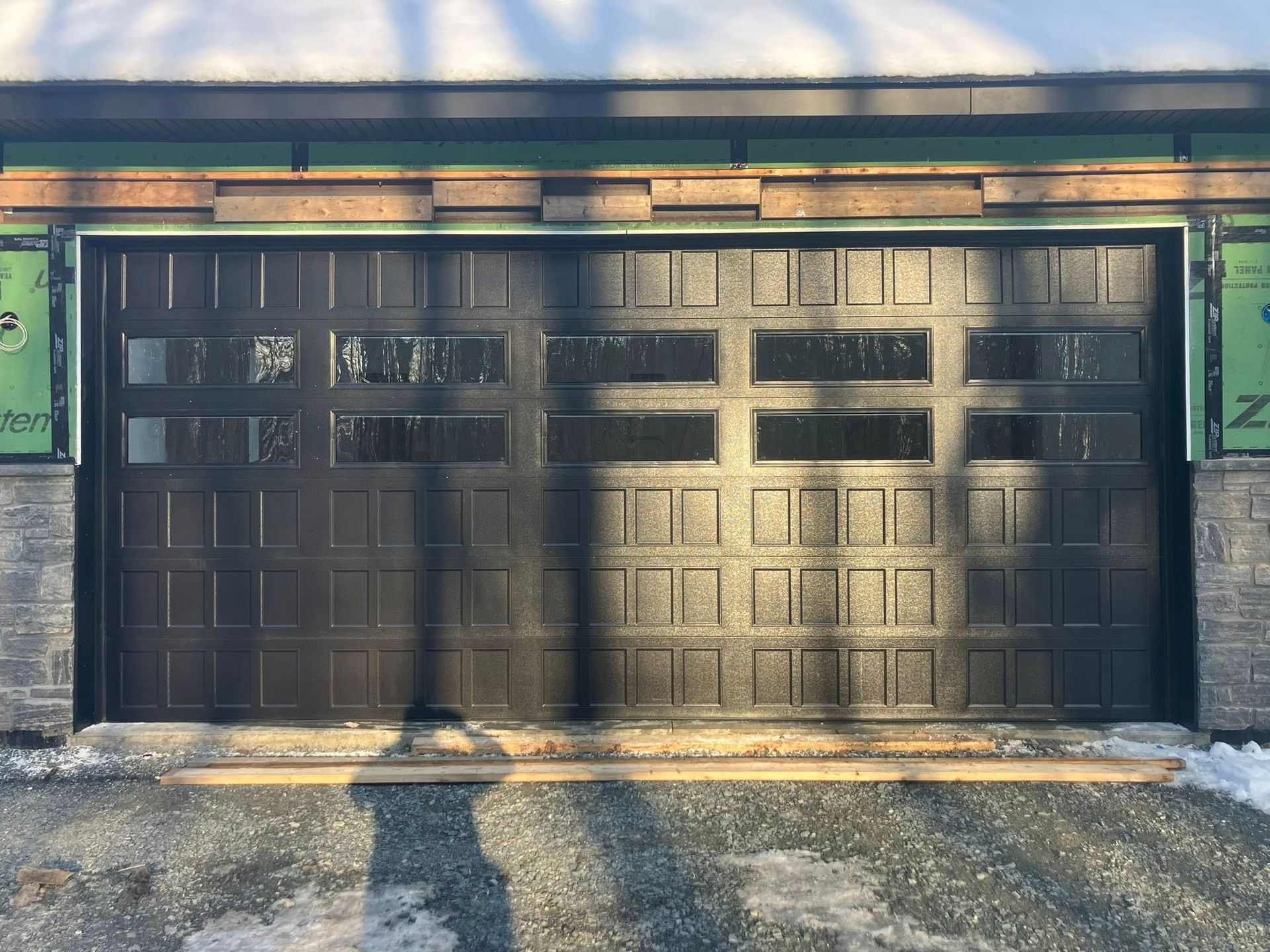 Dark brown garage door with window panels, in front of a building with stone and wood details.