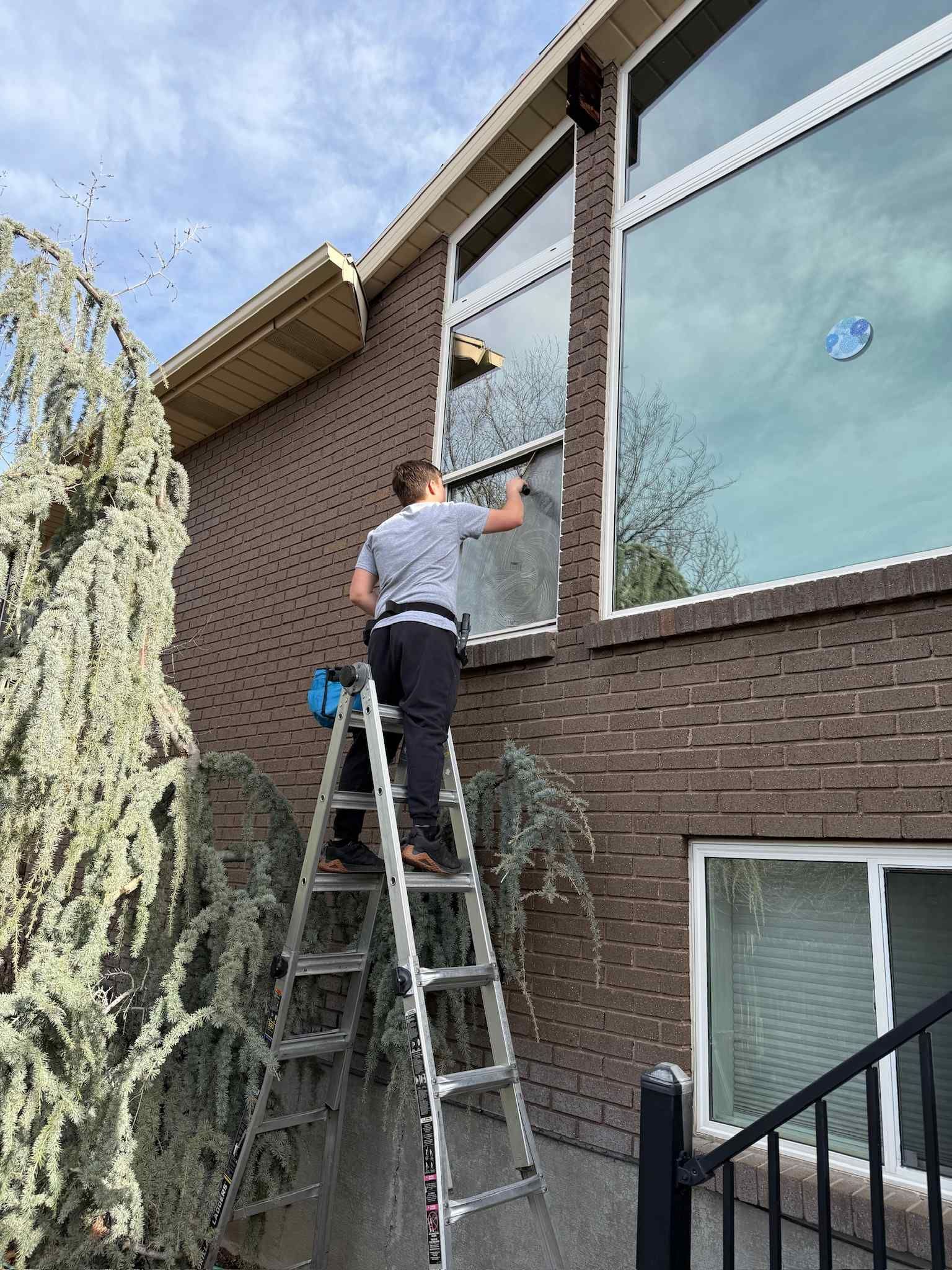 A man is standing on a ladder cleaning a window on a brick building.