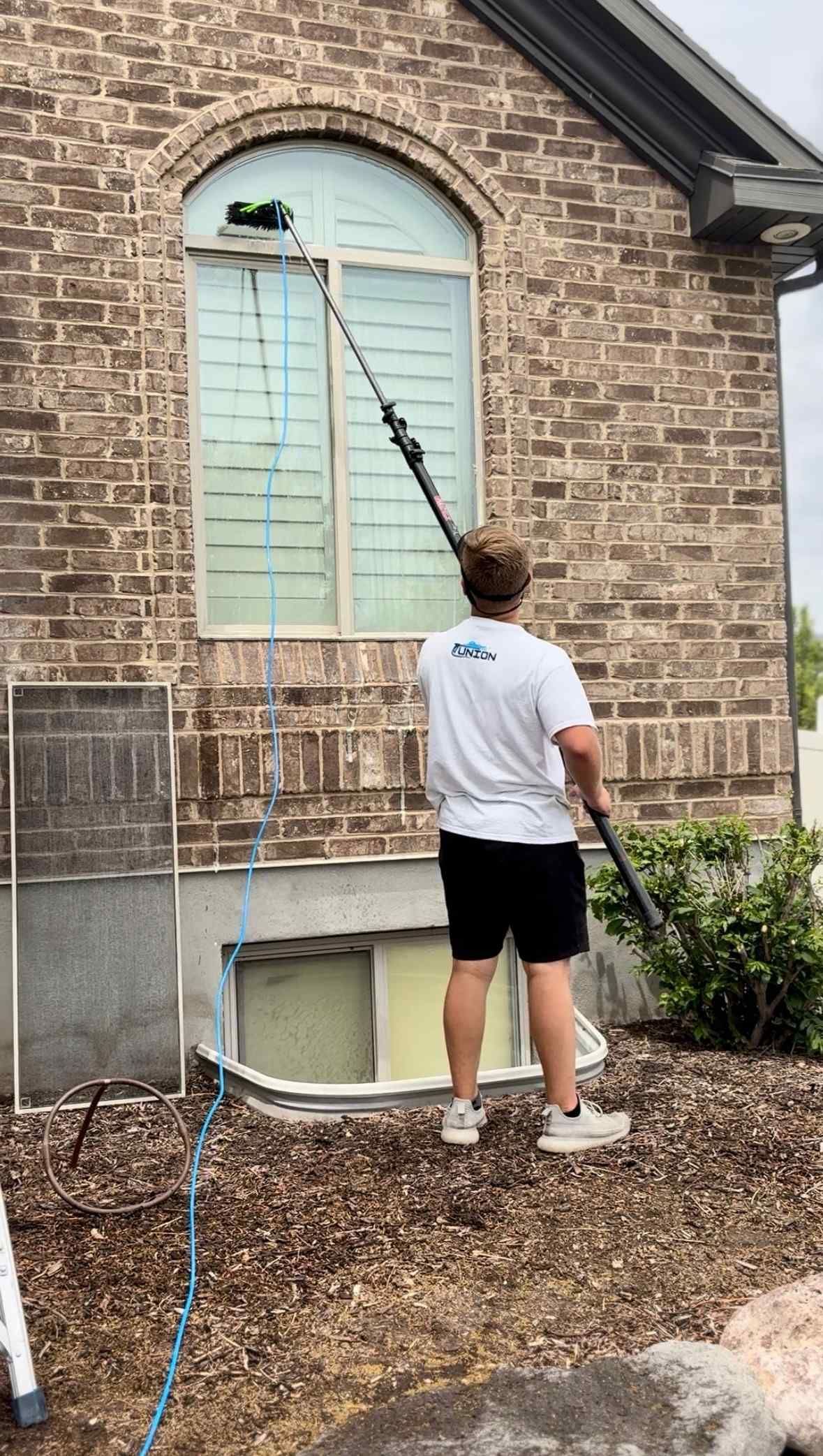 A man is cleaning a window on the side of a brick building.