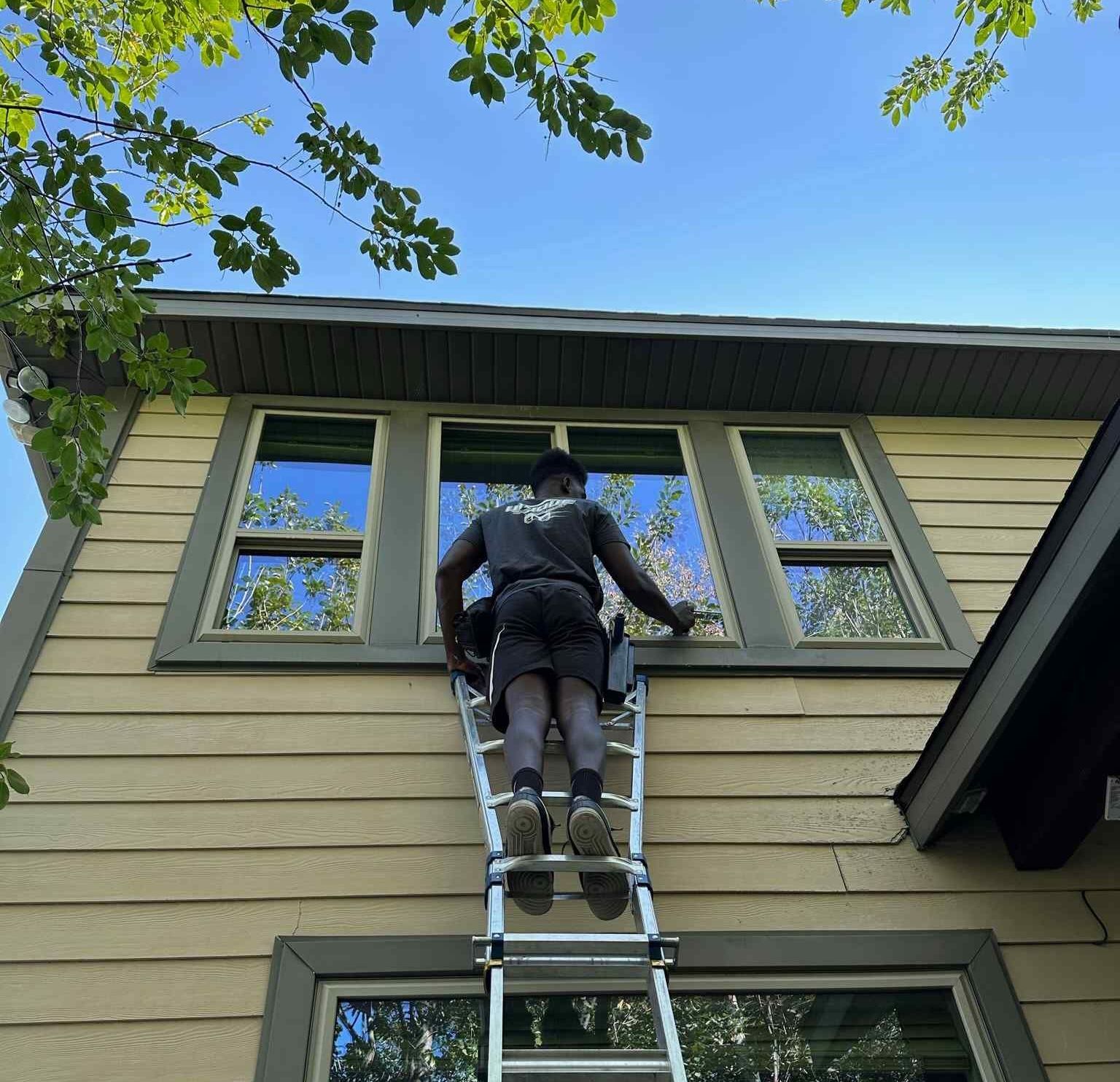 A man is standing on a ladder on the side of a house.