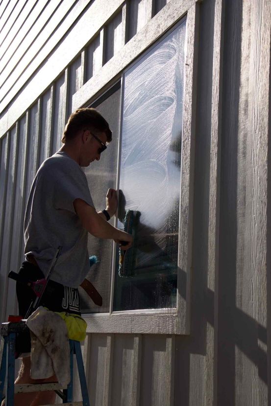 A man is standing on a ladder cleaning a window.