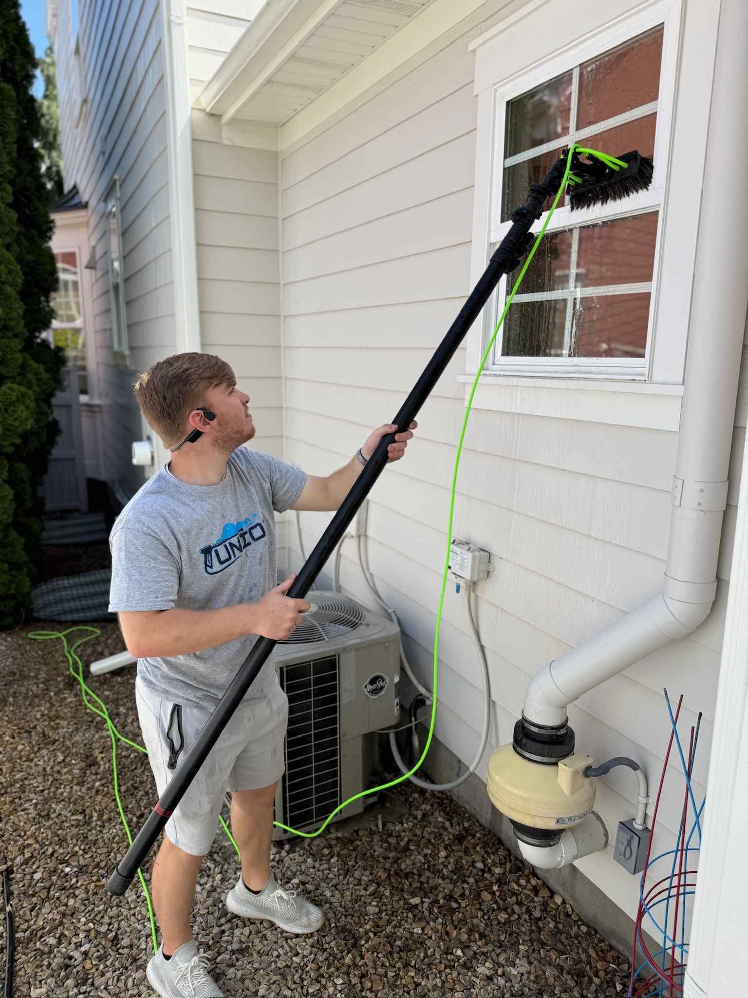 A man is cleaning a window with a long pole.