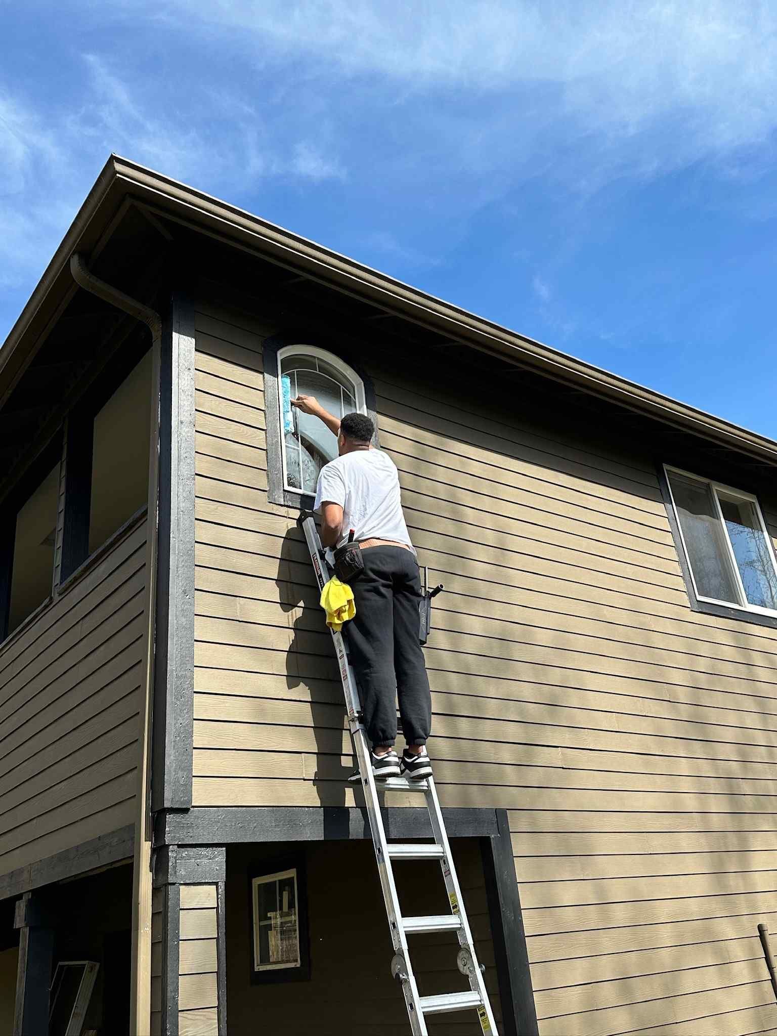 A man is standing on a ladder cleaning a window on the side of a building.