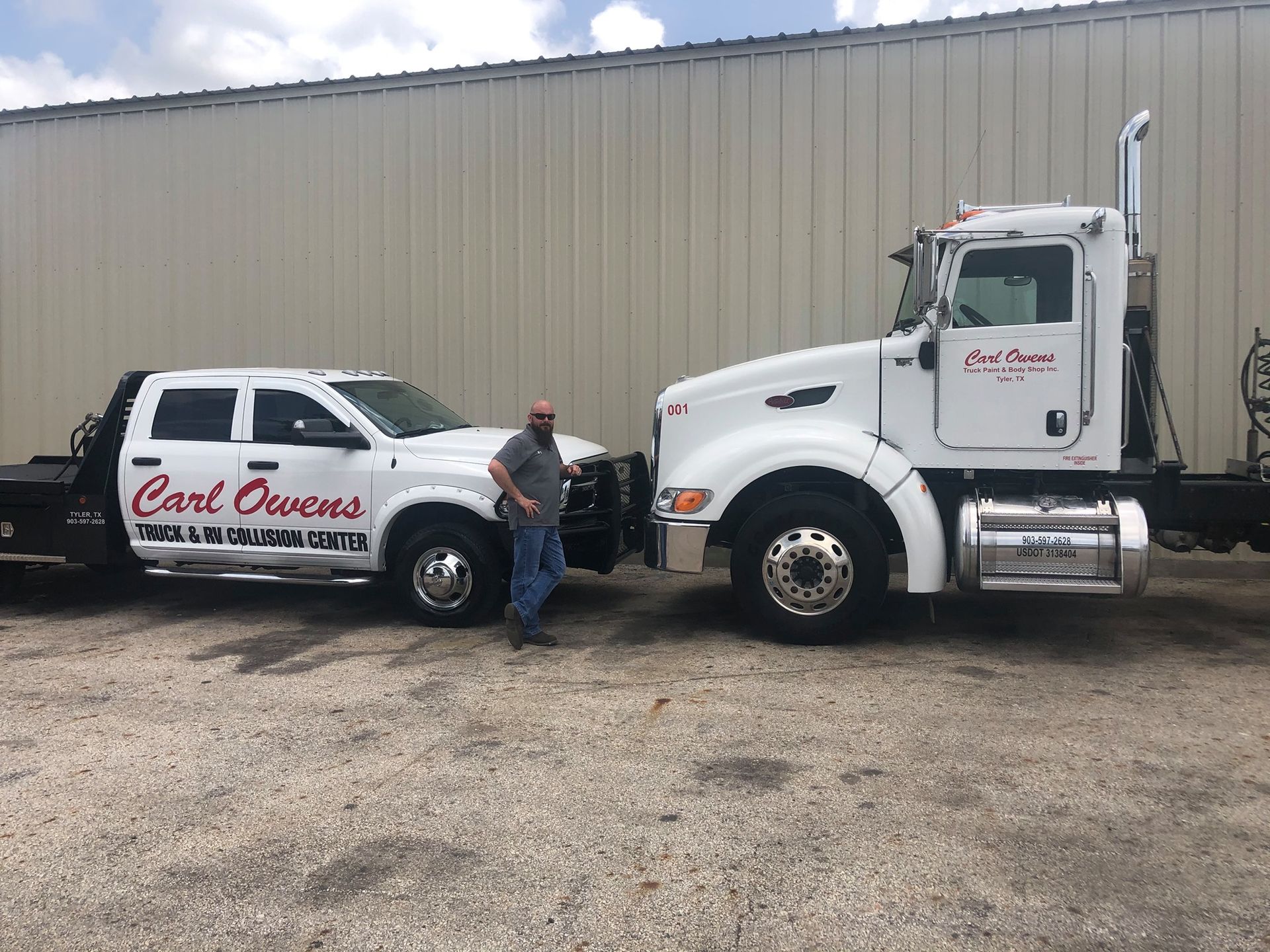 Man standing between a white pickup and a white semi-truck, both with the same company logo, parked outside a warehouse.