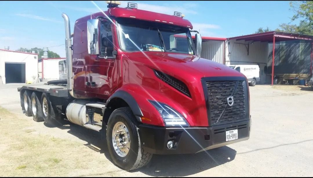 Red Volvo semi-truck parked in front of a building on a sunny day.