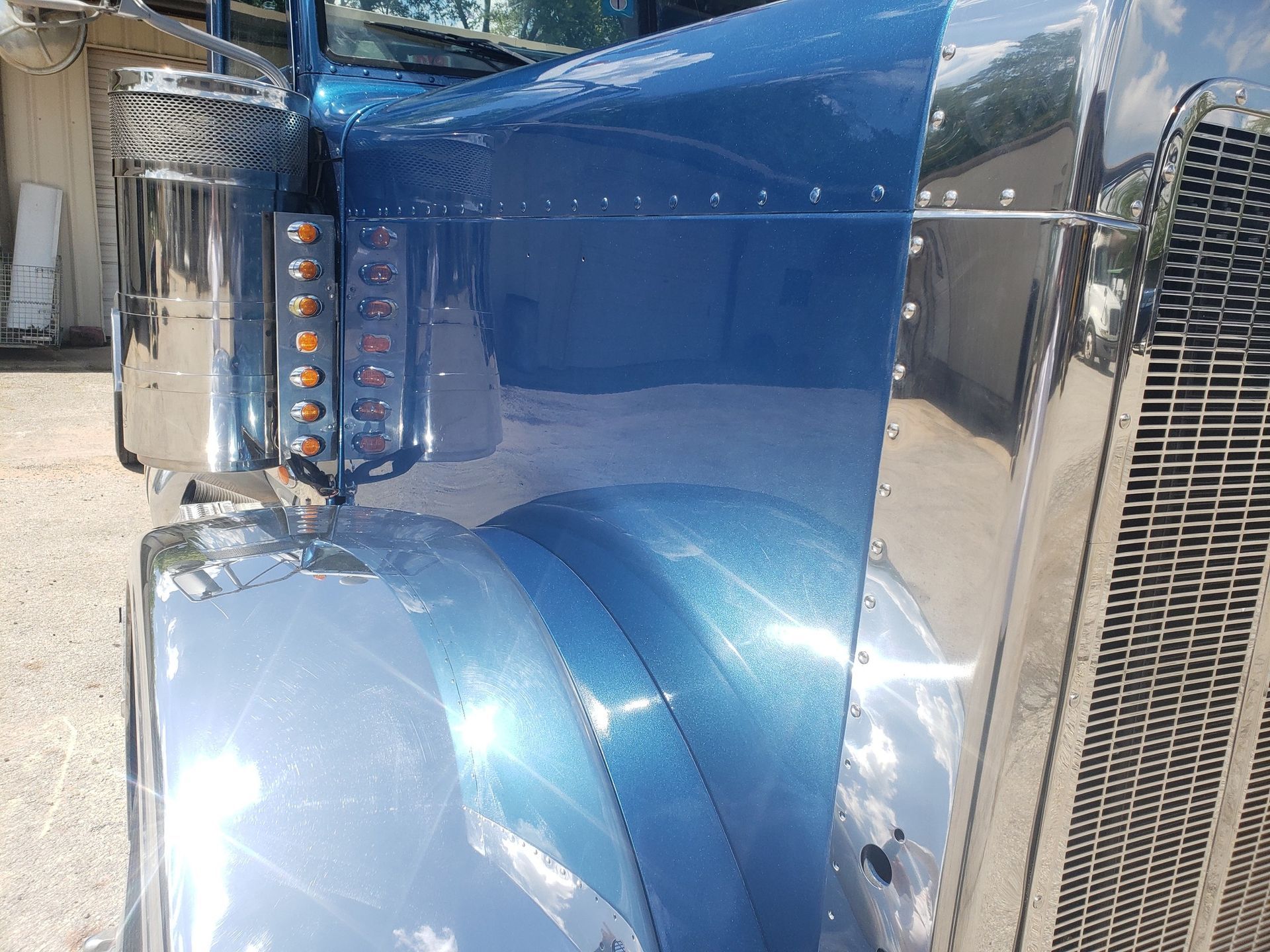 Blue semi-truck cab with chrome details and lights. Sunlight reflects off the shiny surfaces.