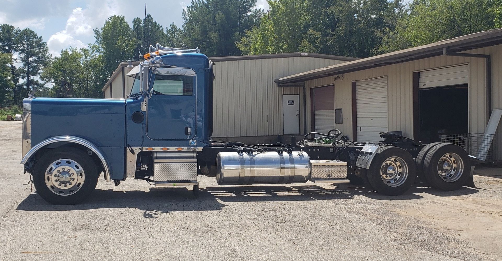 Blue semi-truck parked next to a white industrial building on a sunny day.