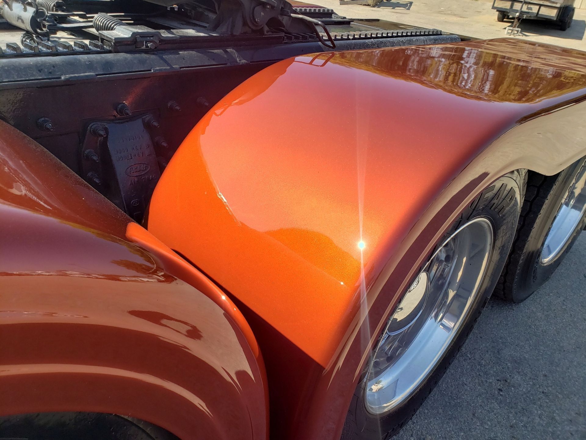 Orange-painted truck fender with chrome wheels, reflecting sunlight.