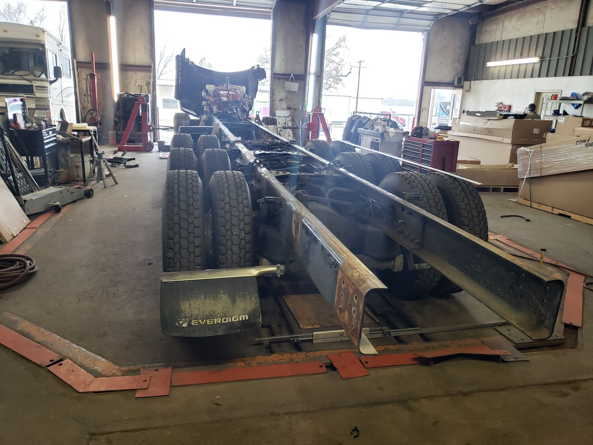A truck chassis on a garage floor; the truck's wheels are visible. The setting is indoors.