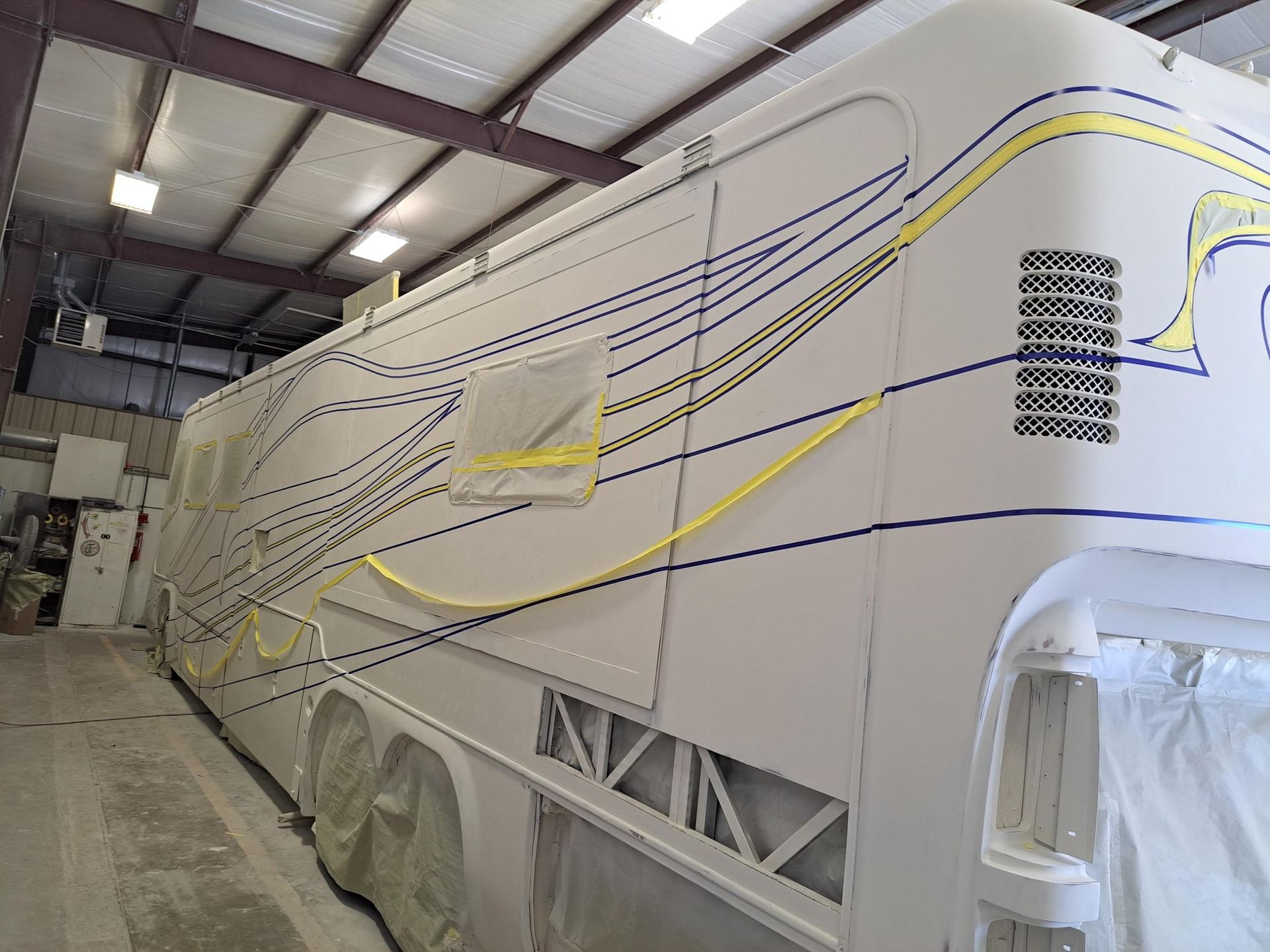 White RV with blue and yellow design lines in a workshop.