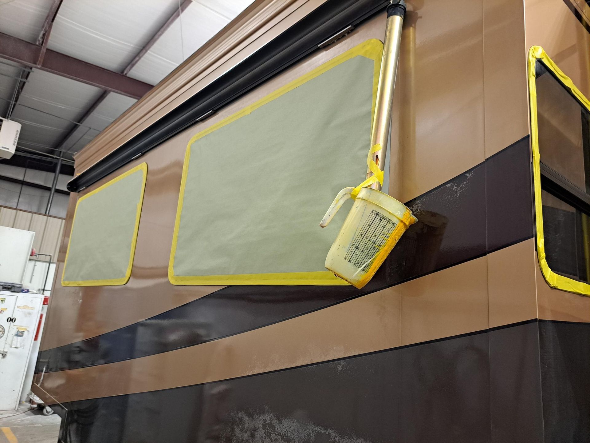 RV exterior with windows masked with yellow tape, paint bucket hanging.