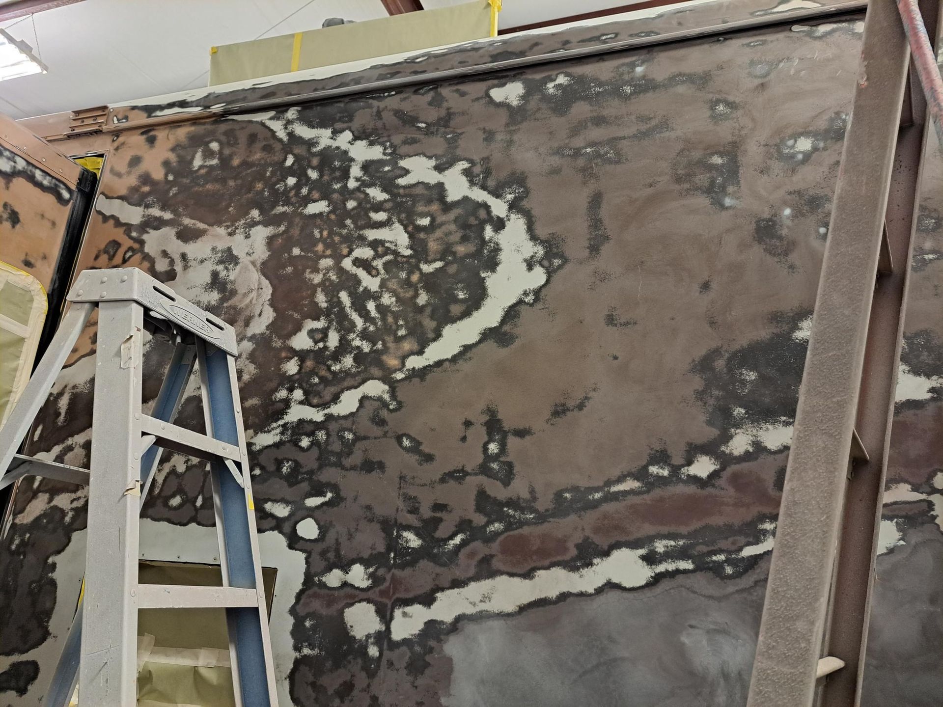 Wall under construction with patches of filler and exposed material. A ladder is in the foreground.