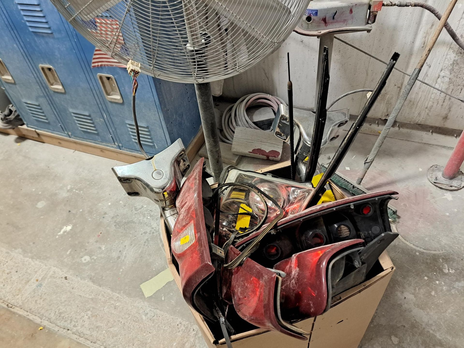 Cardboard box overflowing with car parts under a fan, next to a blue building model.