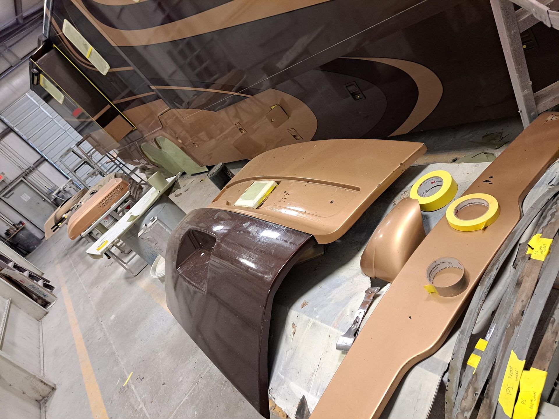 Parts of a vehicle painted brown and gold in a workshop.