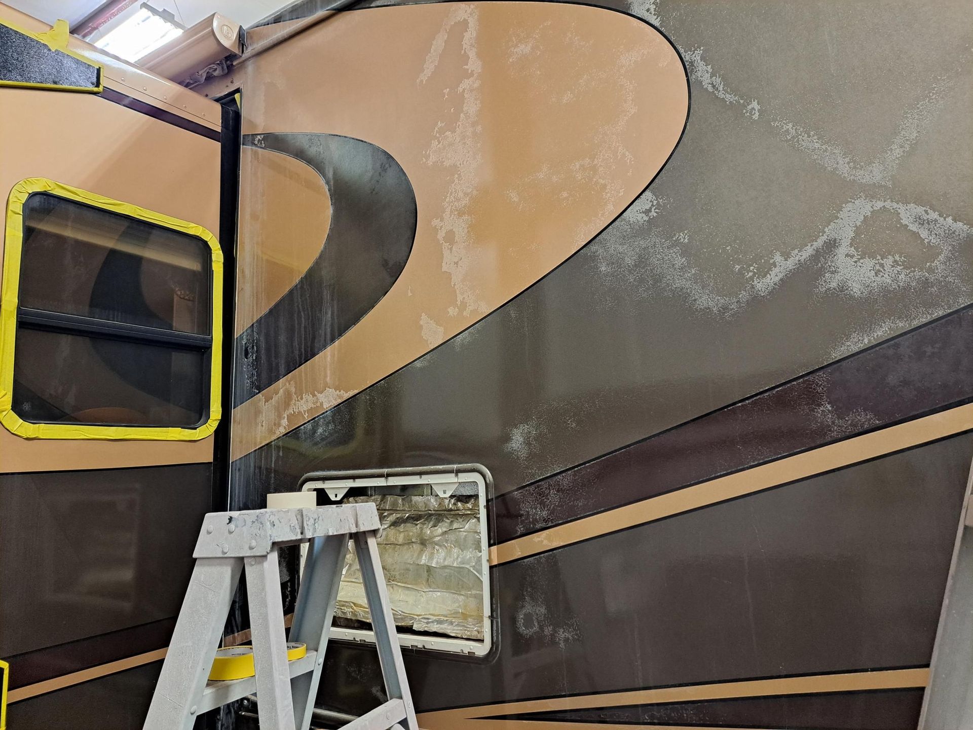 RV exterior with peeling paint and open compartment; a stepladder is present.