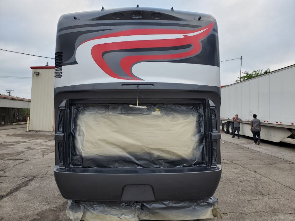 Rear view of a bus with grey, white, and red design, back storage area covered, two people in the background.