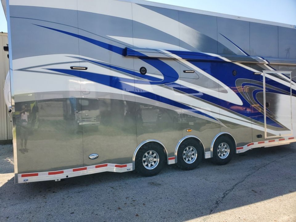 Silver and blue racing trailer parked on pavement, three axles.
