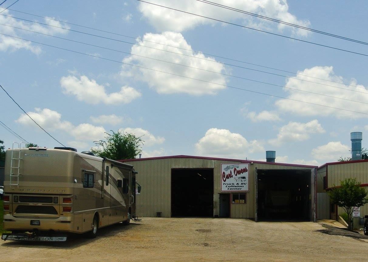RV parked in front of auto repair shop with open bays, under a partly cloudy sky.