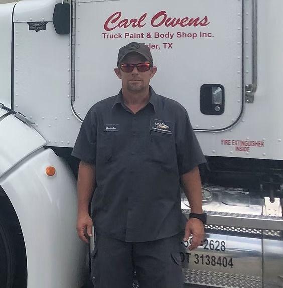 Man in grey uniform and sunglasses, standing next to a white truck with 