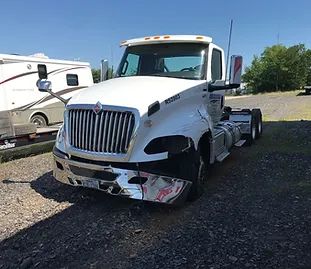 White truck with camper driving on a dirt road through a forest.