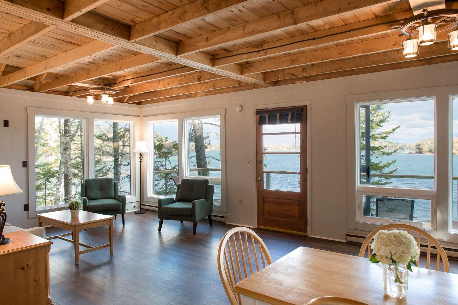 Living room with lake view, wood ceiling and floors, green armchairs, and dining area.