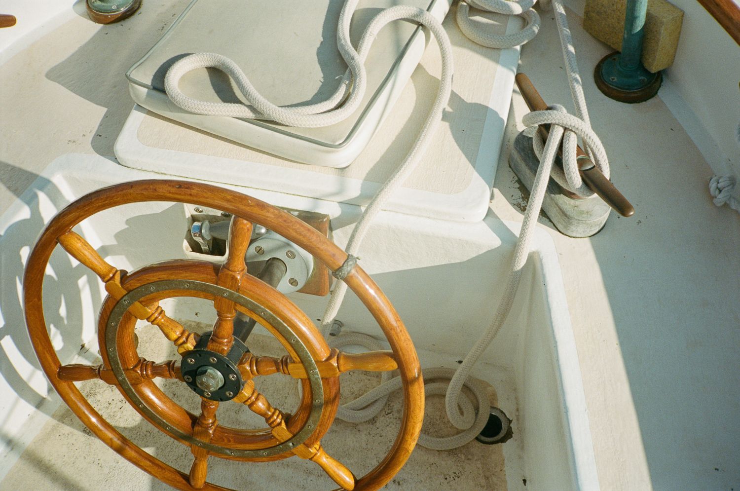 Wooden ship's wheel with ropes and a cleat on the deck of a boat.