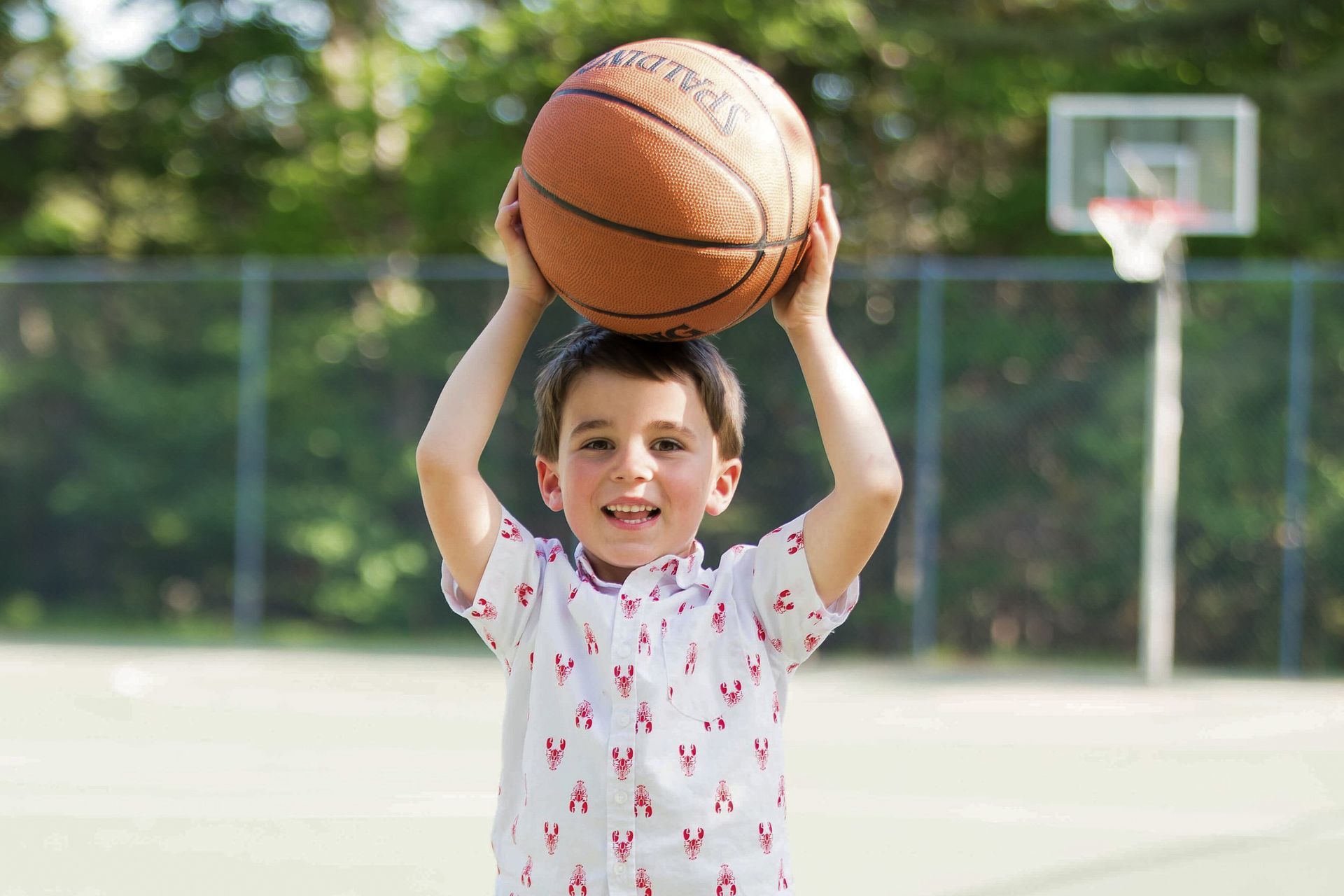 Boy holds a basketball above his head on a basketball court, smiling.