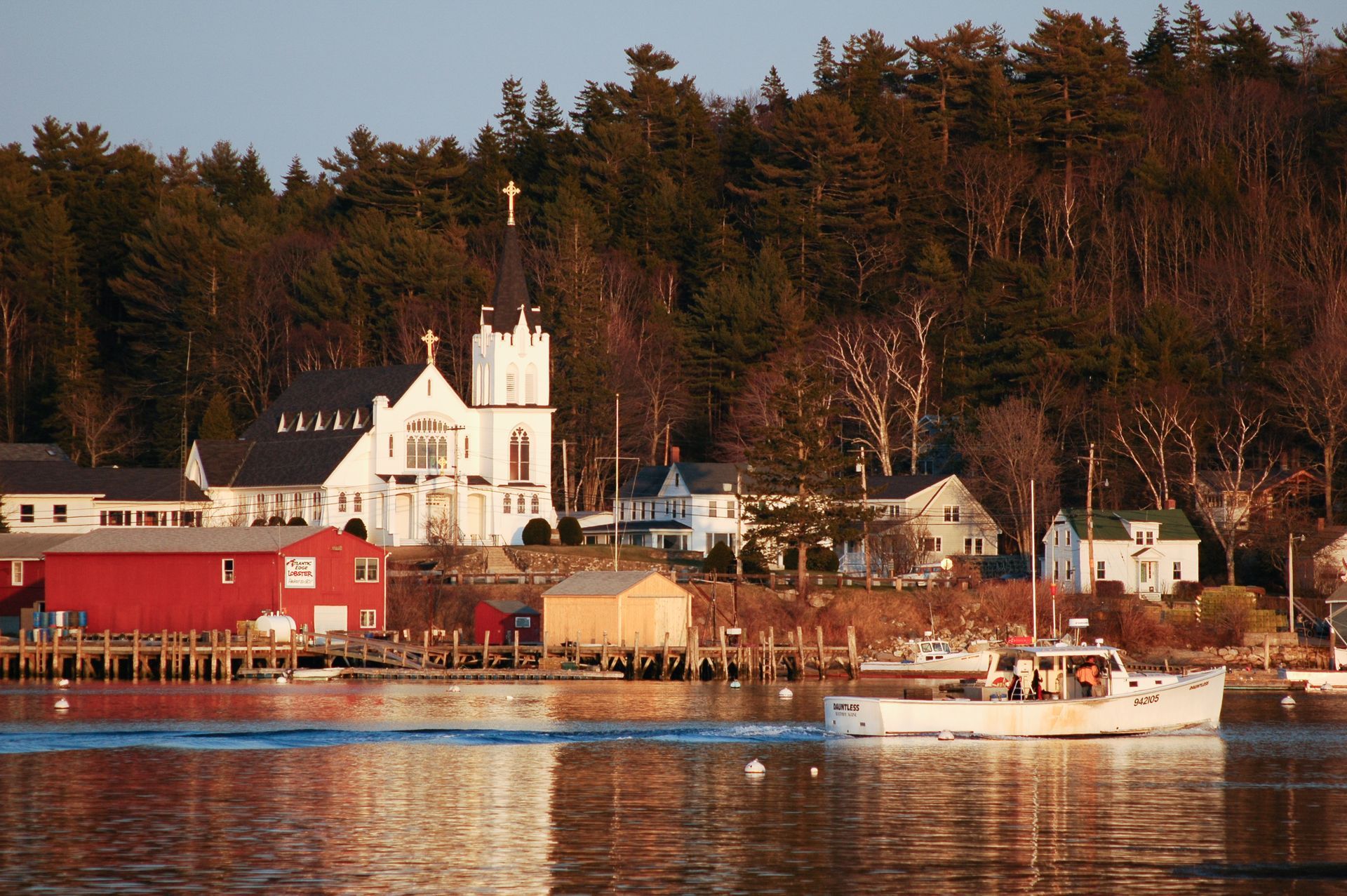 Waterfront view: Church with tall spire, buildings, and a boat on calm water.