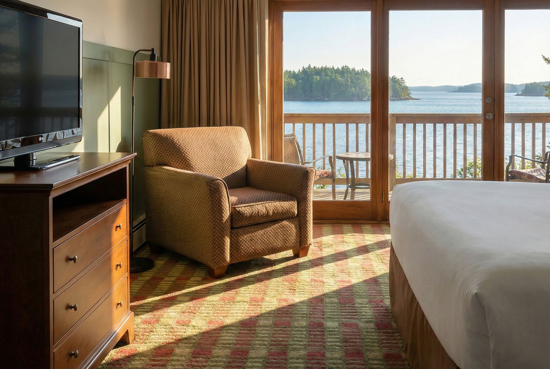 Bedroom with balcony overlooking a lake. A wicker armchair sits near the open doors.