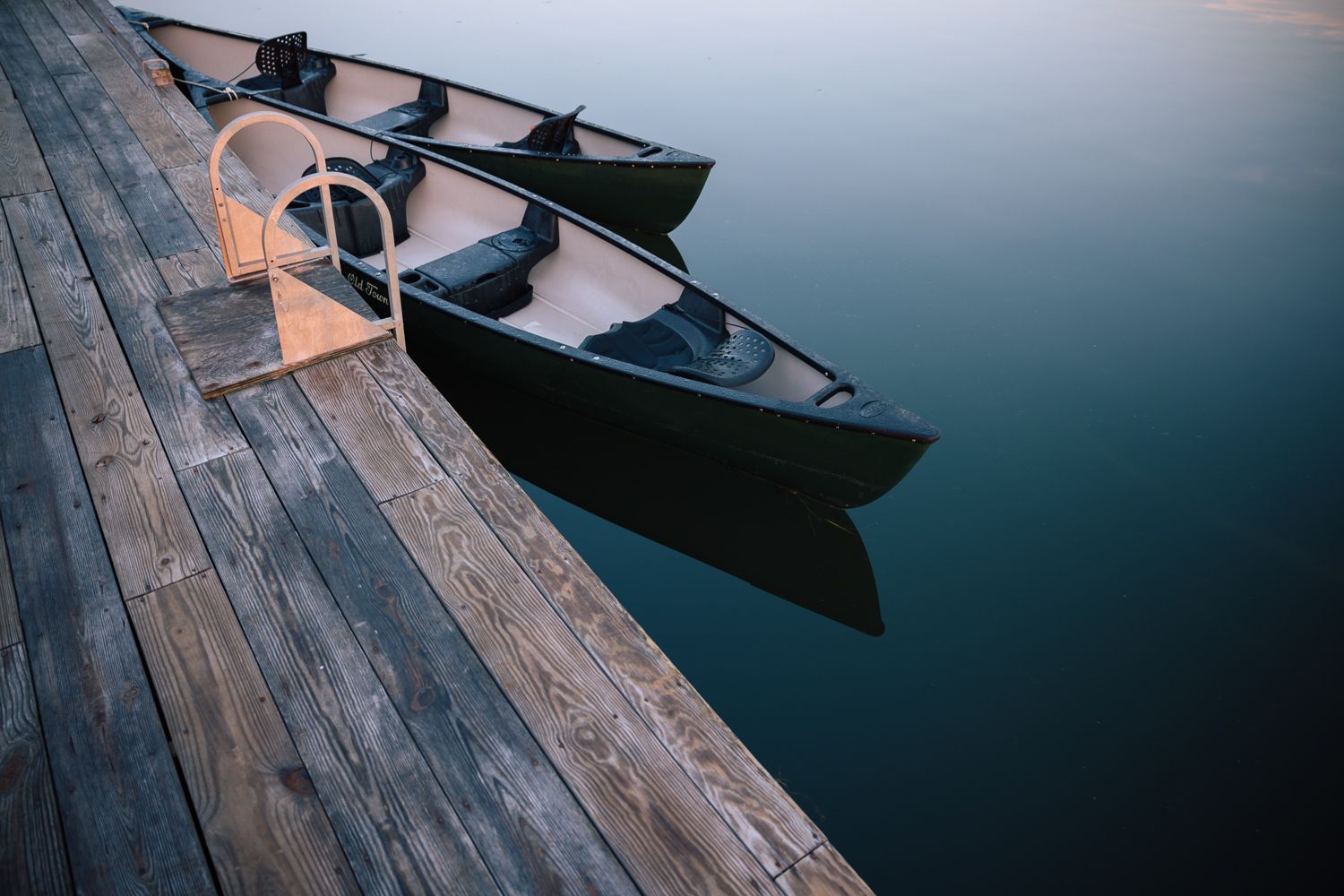 Two canoes docked beside a wooden pier on calm water.