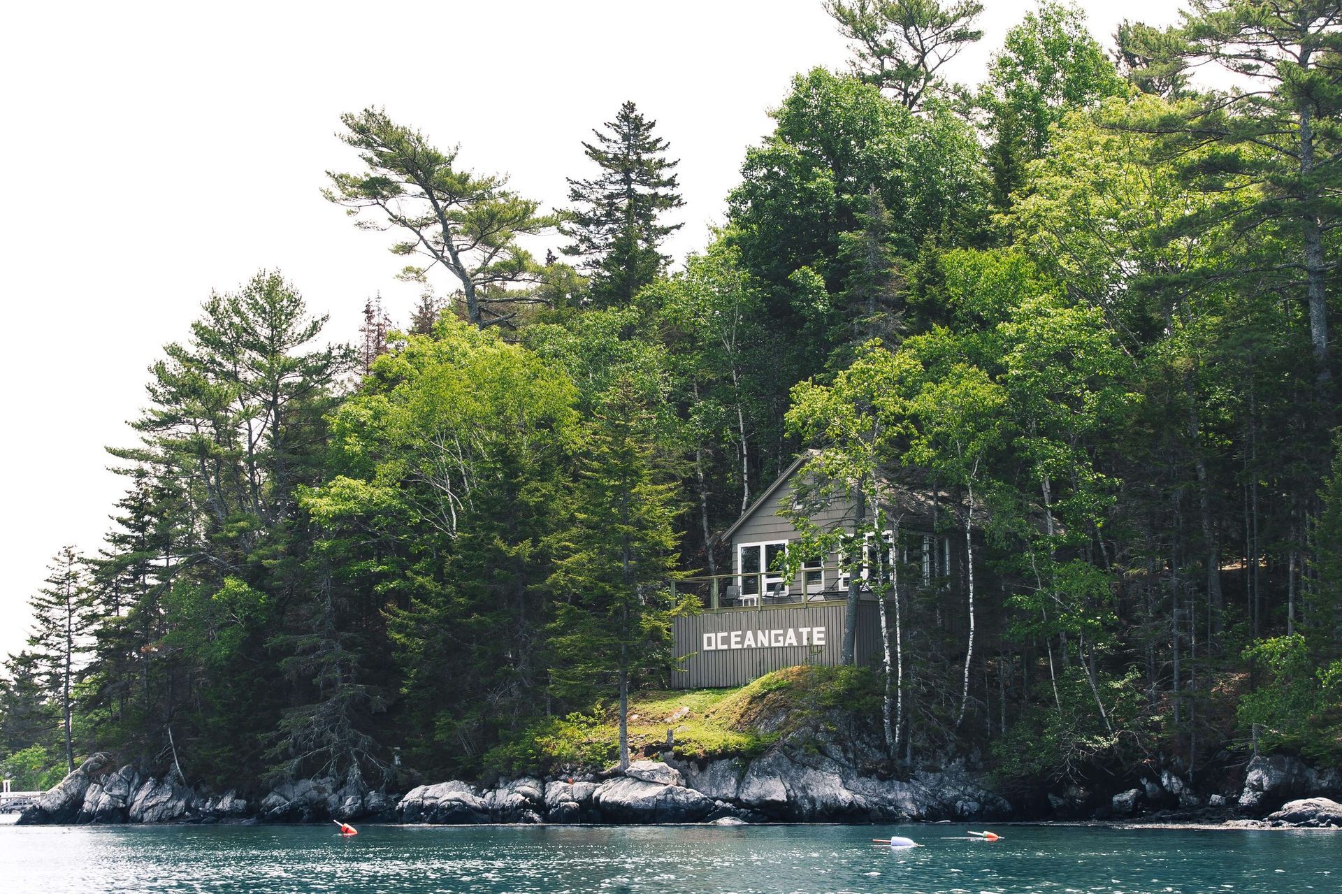 Small cabin nestled in trees on a rocky island, viewed from water.