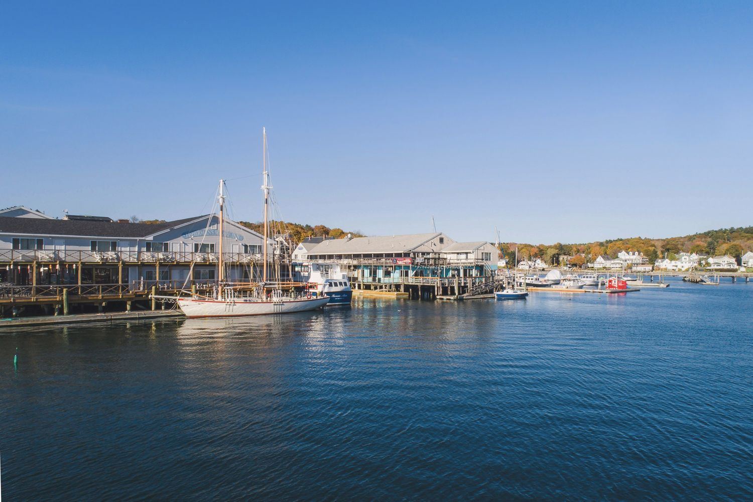 Harbor scene with boats docked near buildings under a clear blue sky.