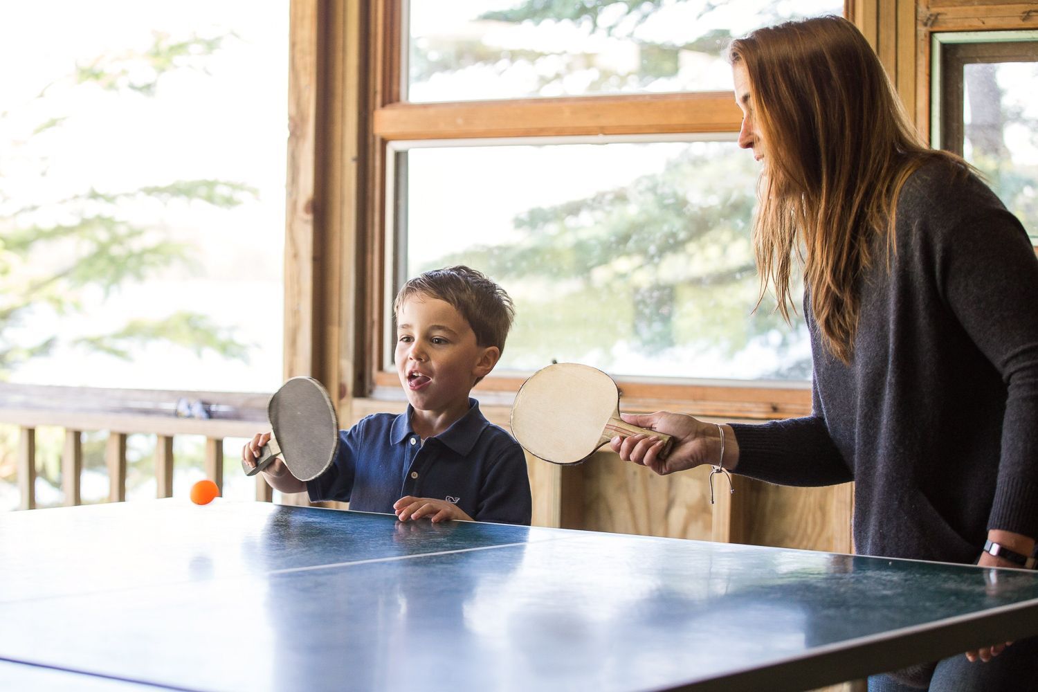 Woman and child playing table tennis indoors, ball in mid-air.