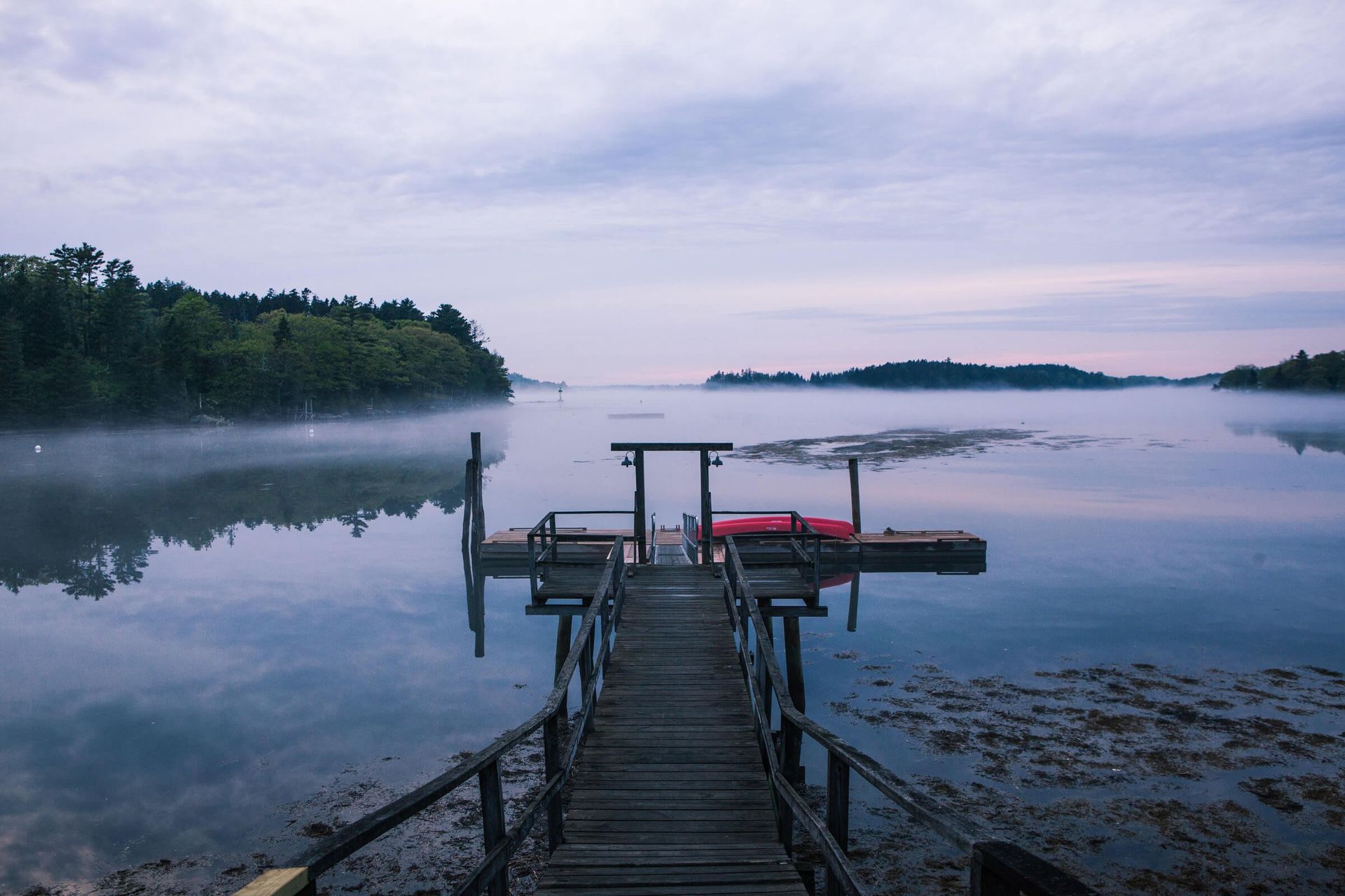 Wooden pier extending into calm water with morning mist and distant trees.