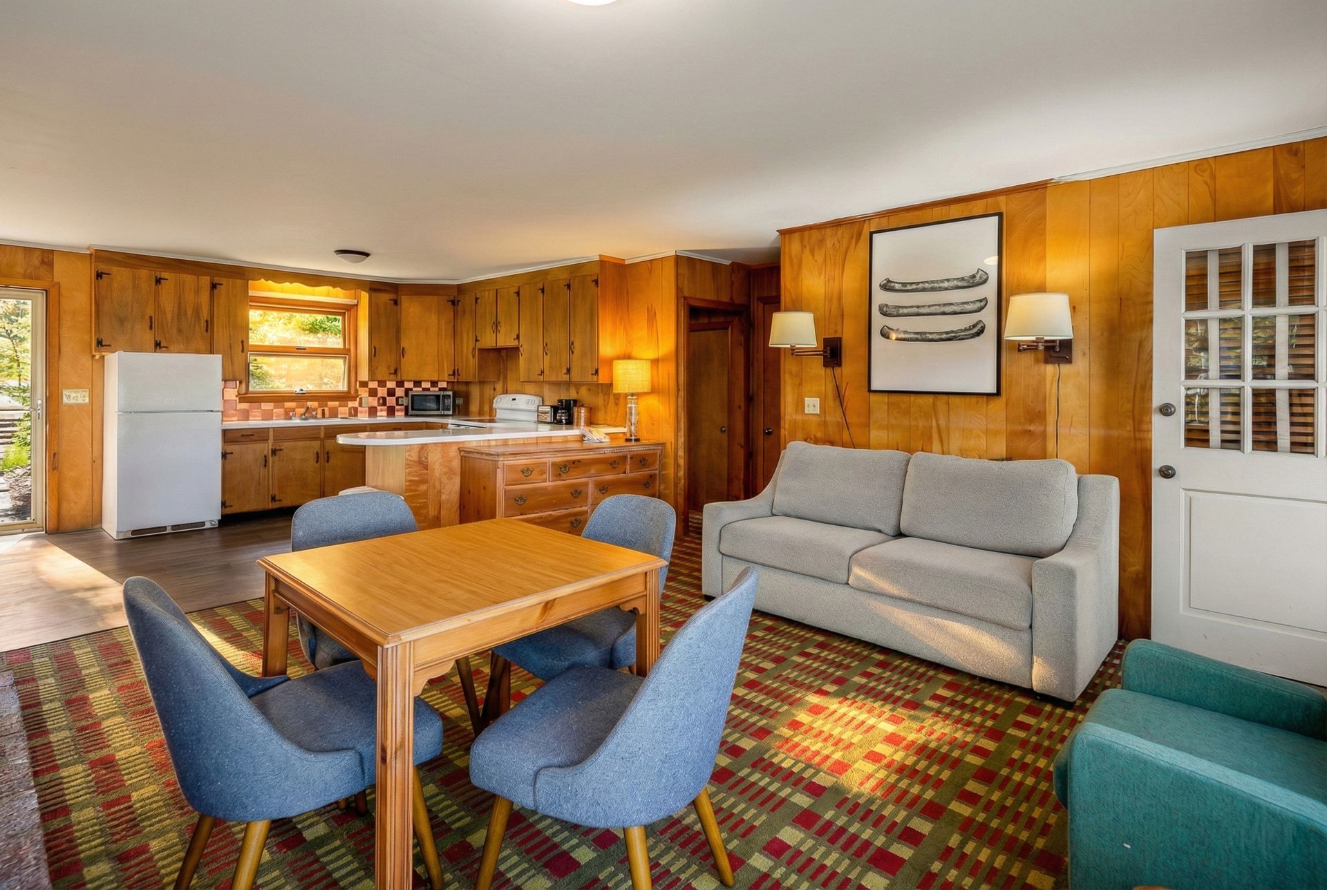 Cozy cabin interior: kitchen, dining area with blue chairs, sofa, and teal armchair.