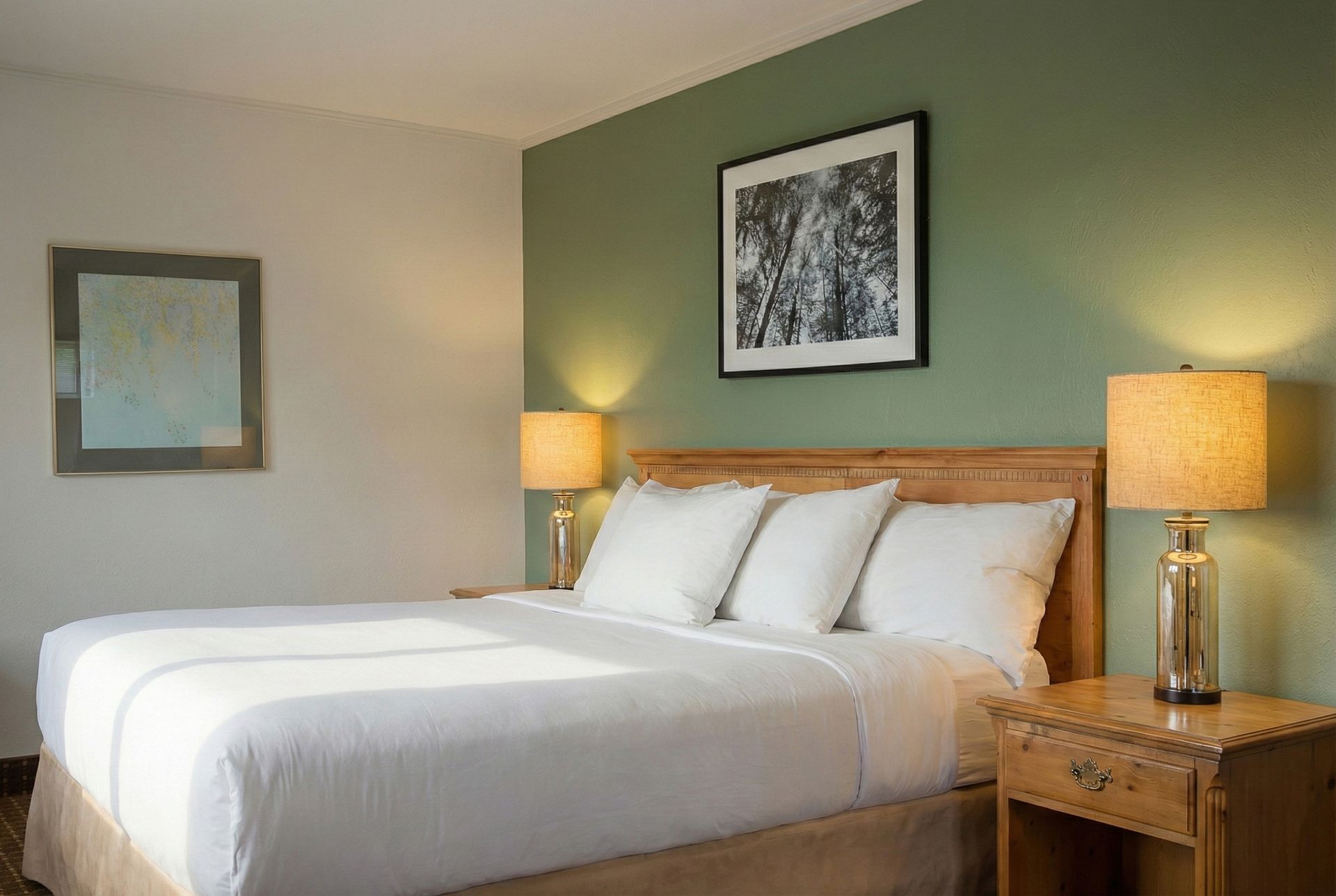Bedroom with a bed, nightstand, lamps, and artwork on a green and white wall.