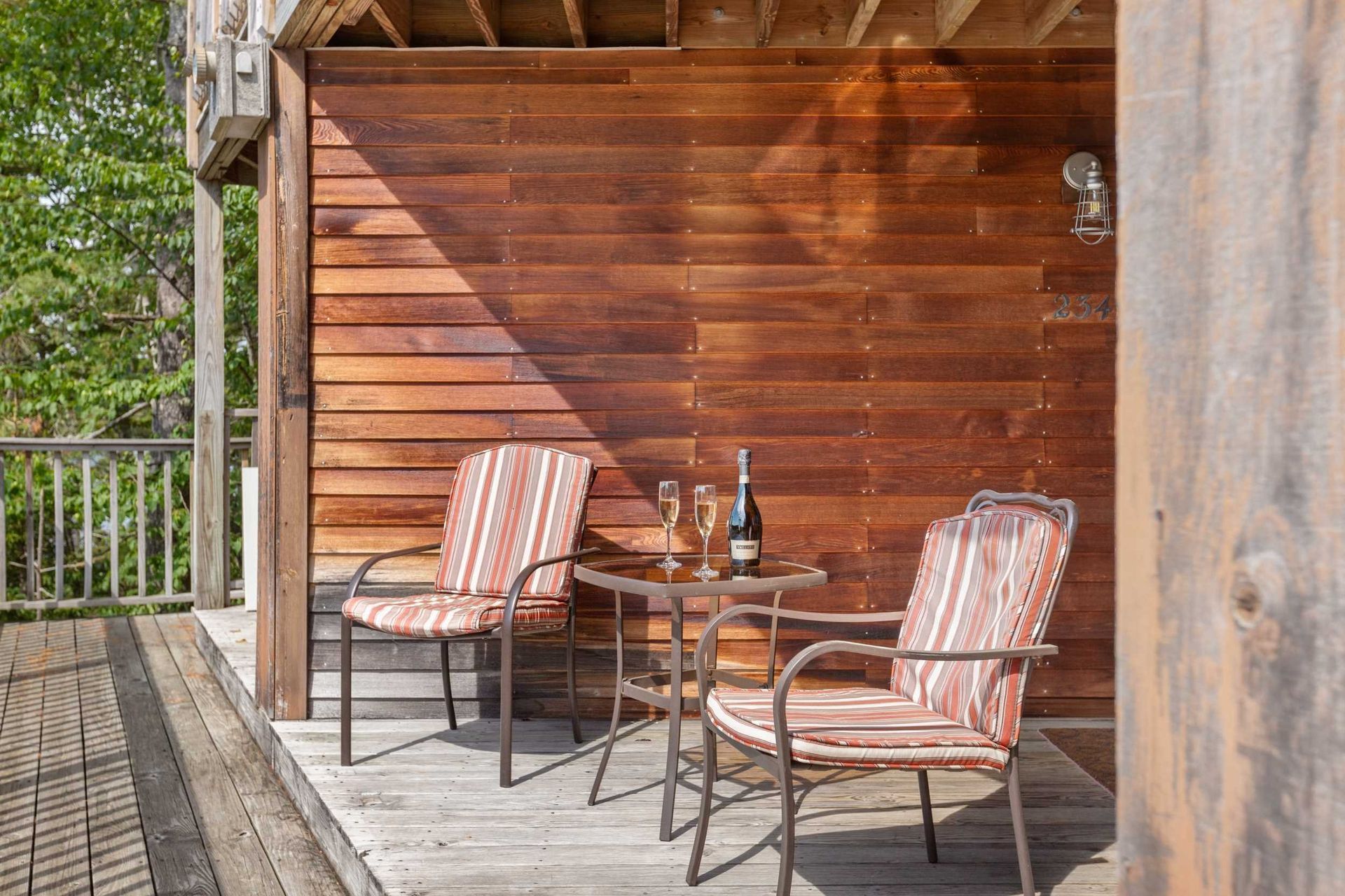 Two chairs and a table with champagne on a wooden deck.