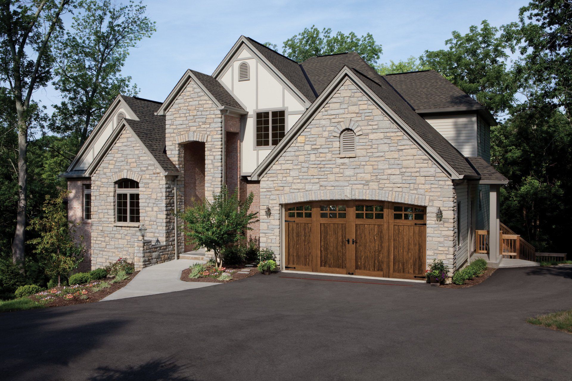 Stone house with a brown garage door, driveway, and landscaping.